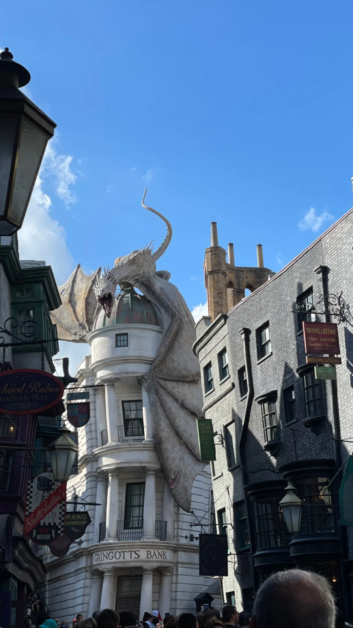 Giant dragon decoration on Gringotts Bank building at a theme park, with surrounding buildings and a crowd of people.