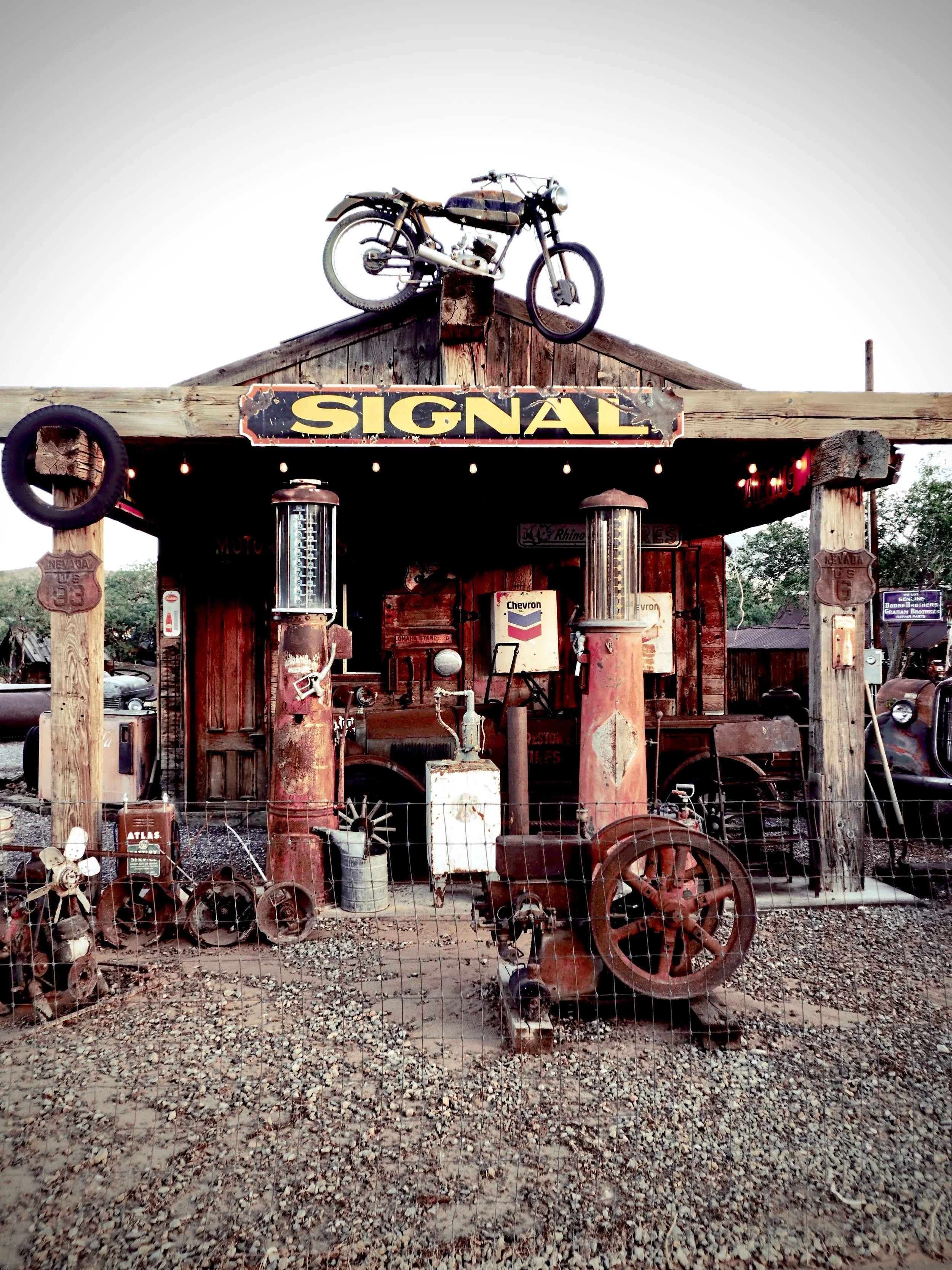 Old vintage gas station with rusty pumps, vintage vehicle on the roof, and rustic wooden structure.