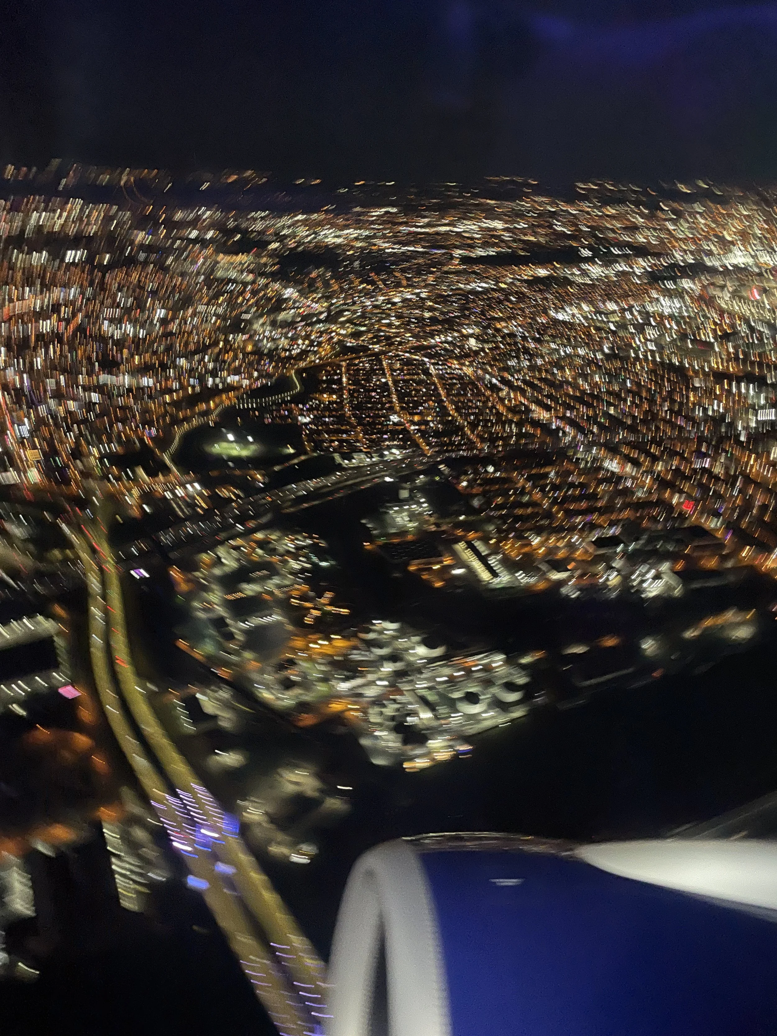 Nighttime aerial photograph of a city with numerous lights, a river running through it, bridges, and tall buildings, taken from an airplane window.
