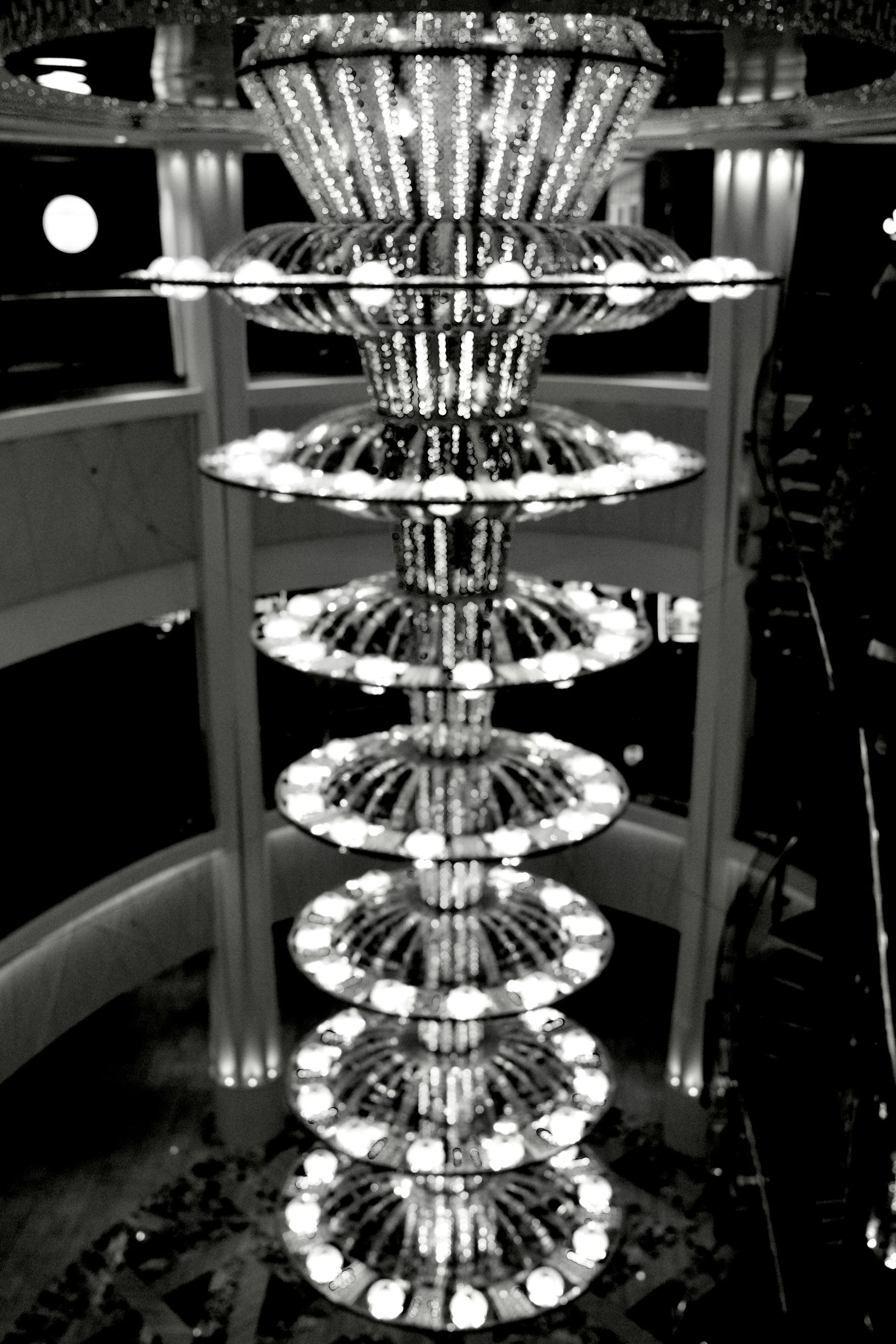 A large, ornate chandelier with multiple tiers of lights, reflecting constellations of lights below in a mirror surface.