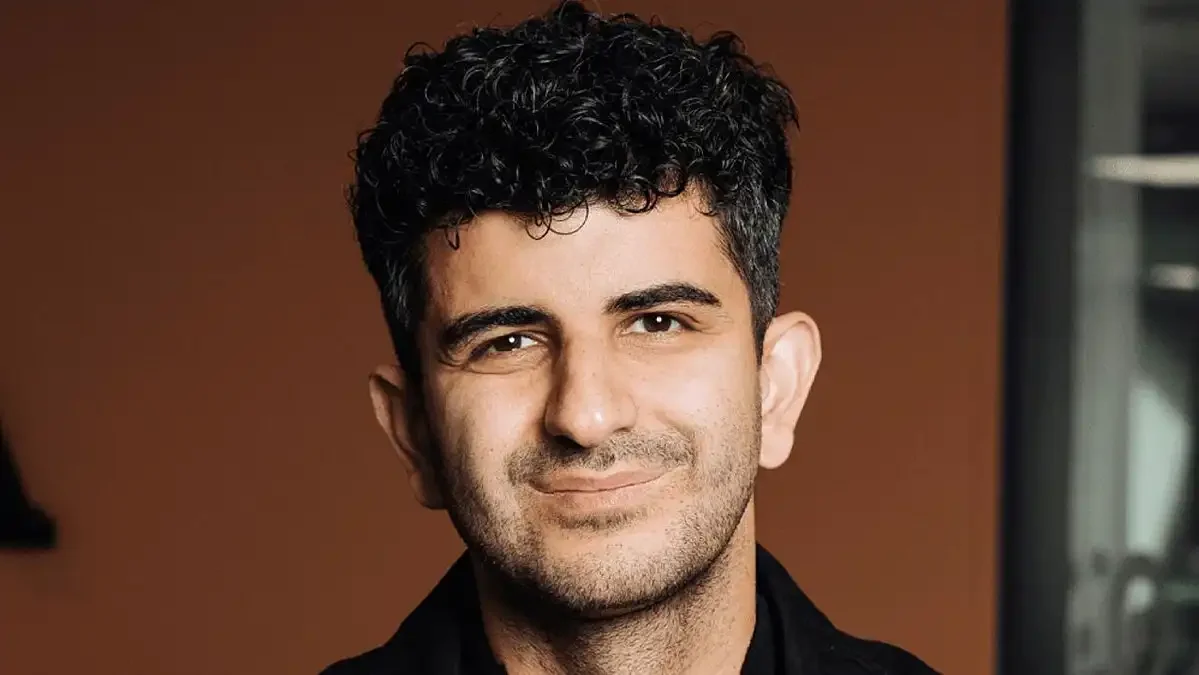 En man med svarta lockiga hår rhyser och tittar på sina ringar på fingrarna.