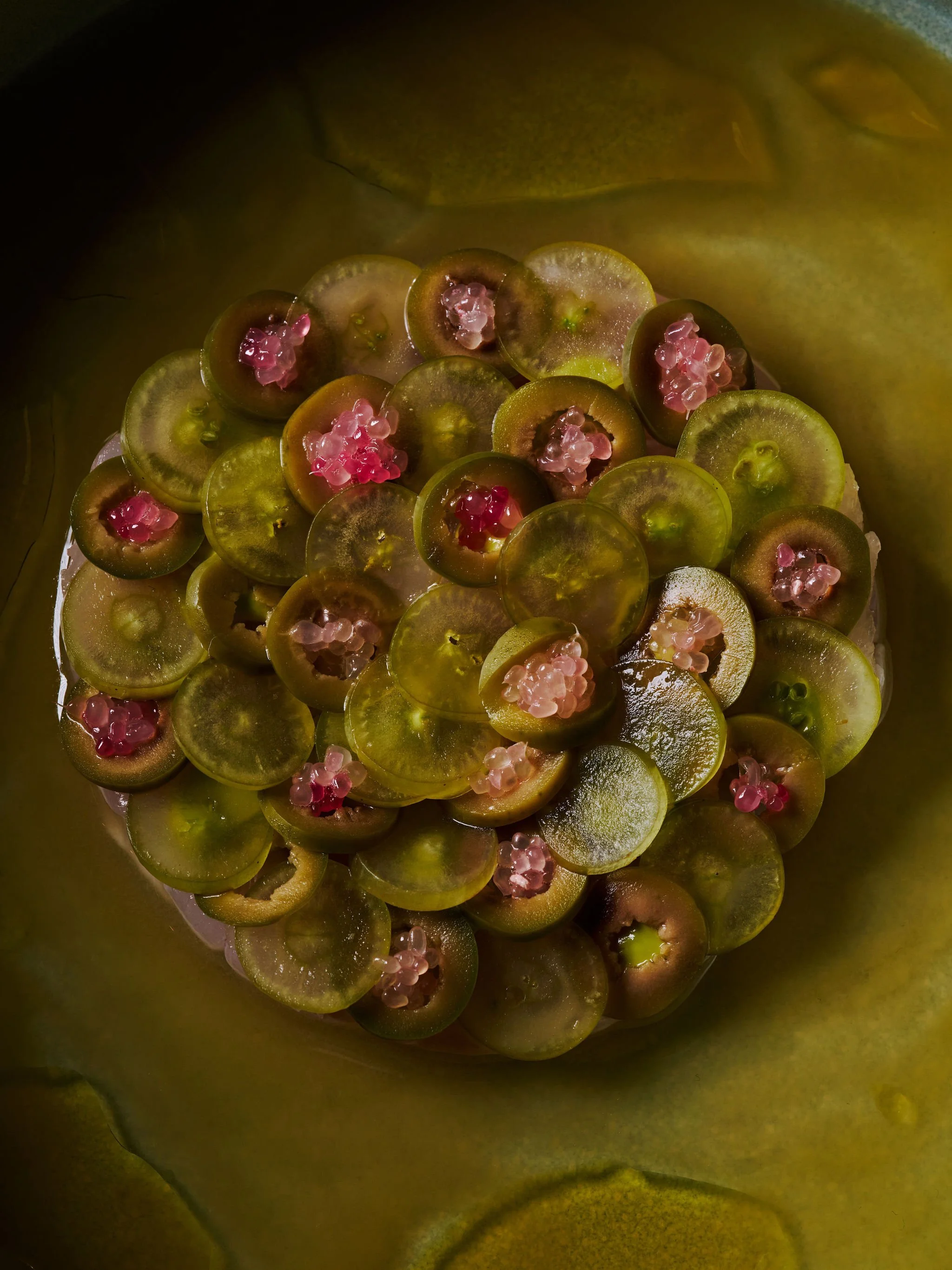 Close-up of small, round green grapes with pinkish seeds inside, placed on a green banana leaf.