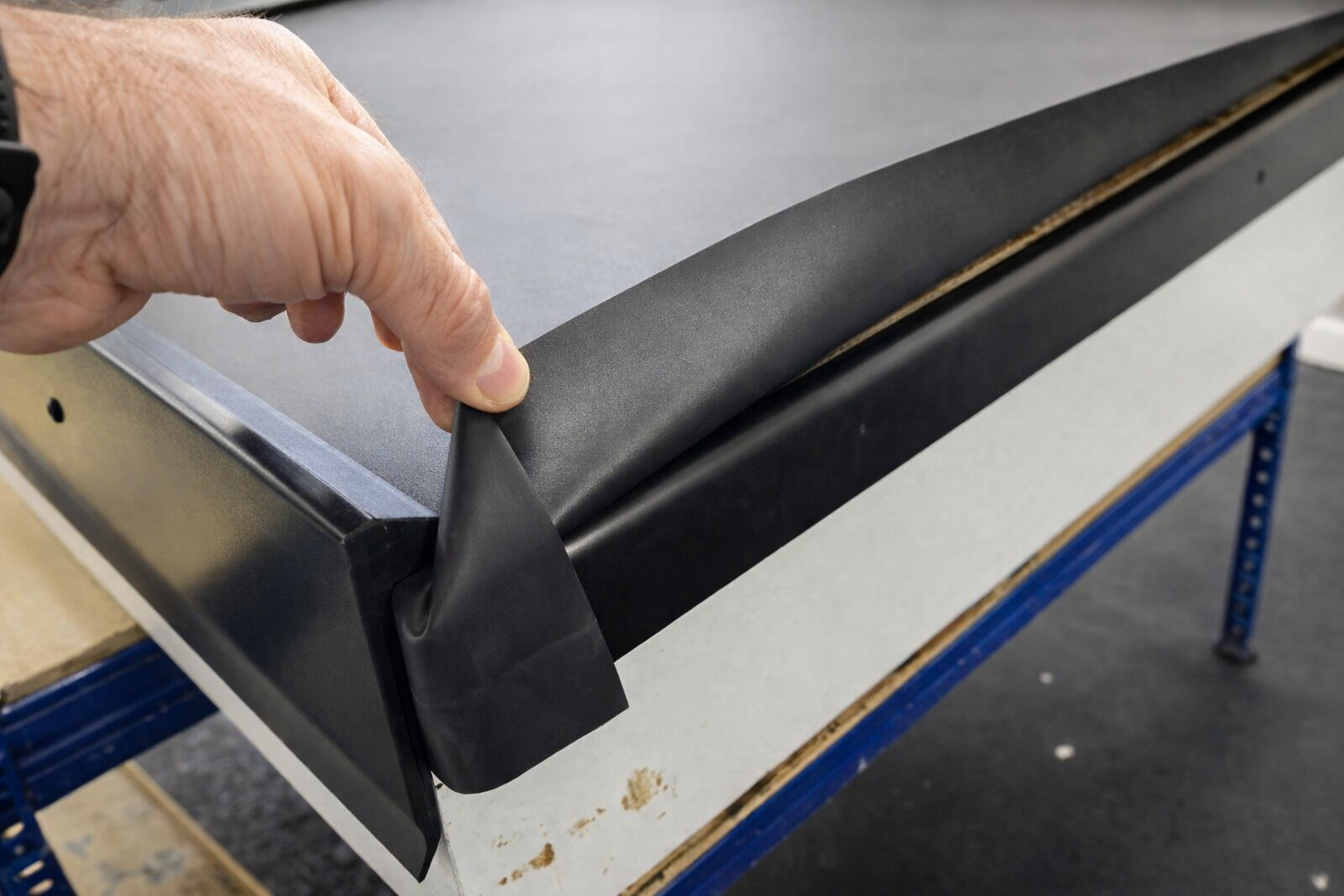 A person peeling a black adhesive rubber strip from a white surface, possibly a countertop or piece of furniture, while working on assembly or maintenance.