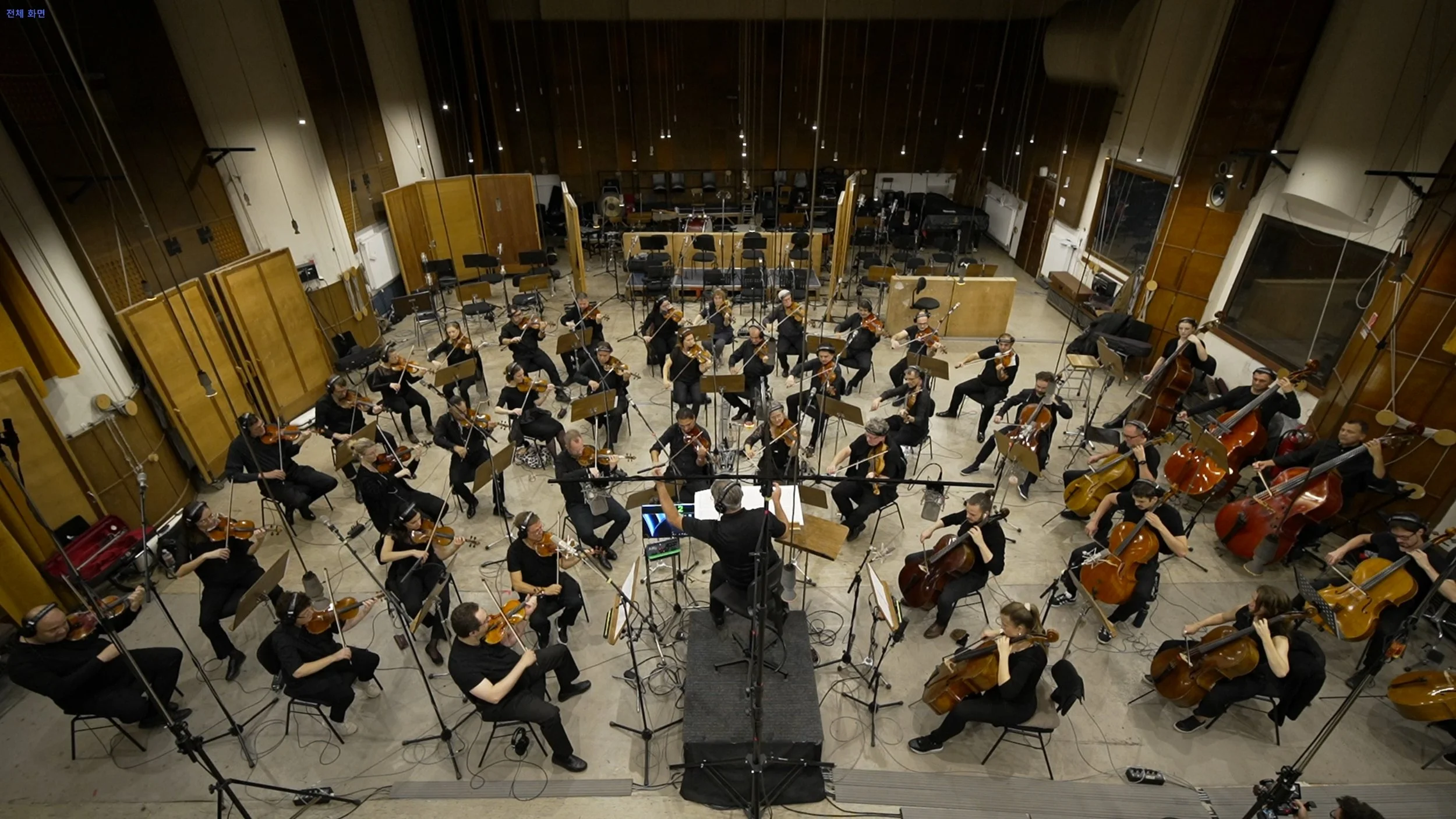 오케스트라 연습실에서 많은 연주자가 악기를 연주하고 지휘자가 지휘하는 모습.