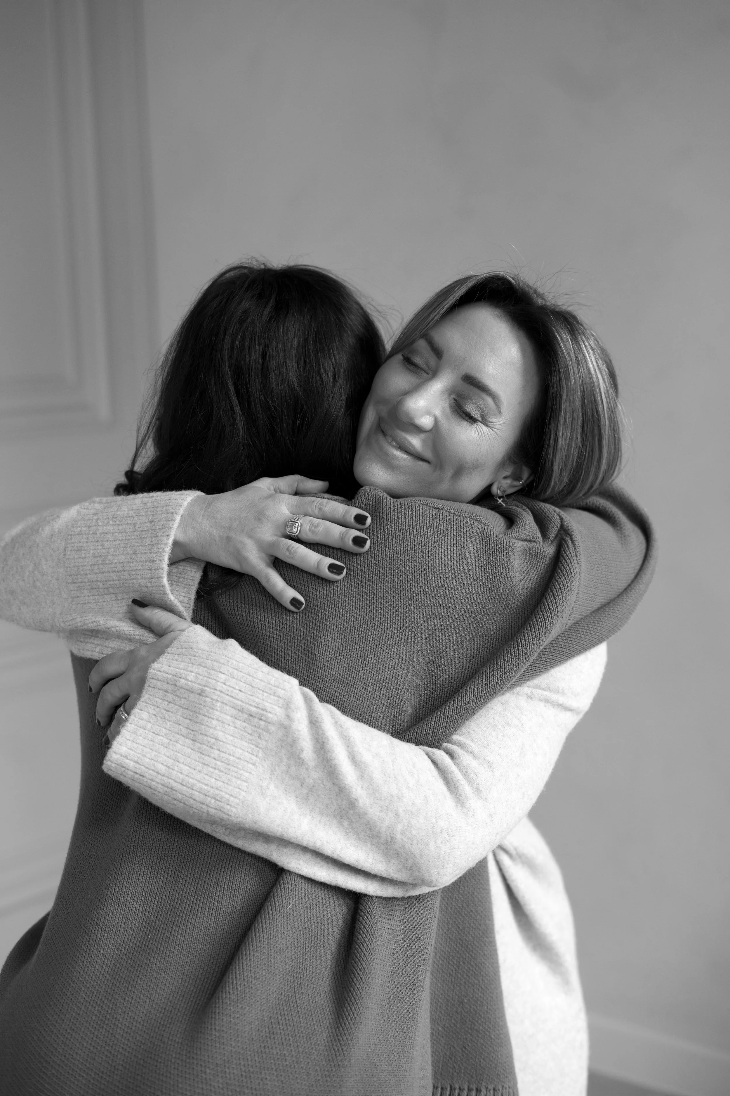 Two women hugging warmly, one with dark hair and the other with light hair, smiling softly in an embrace.