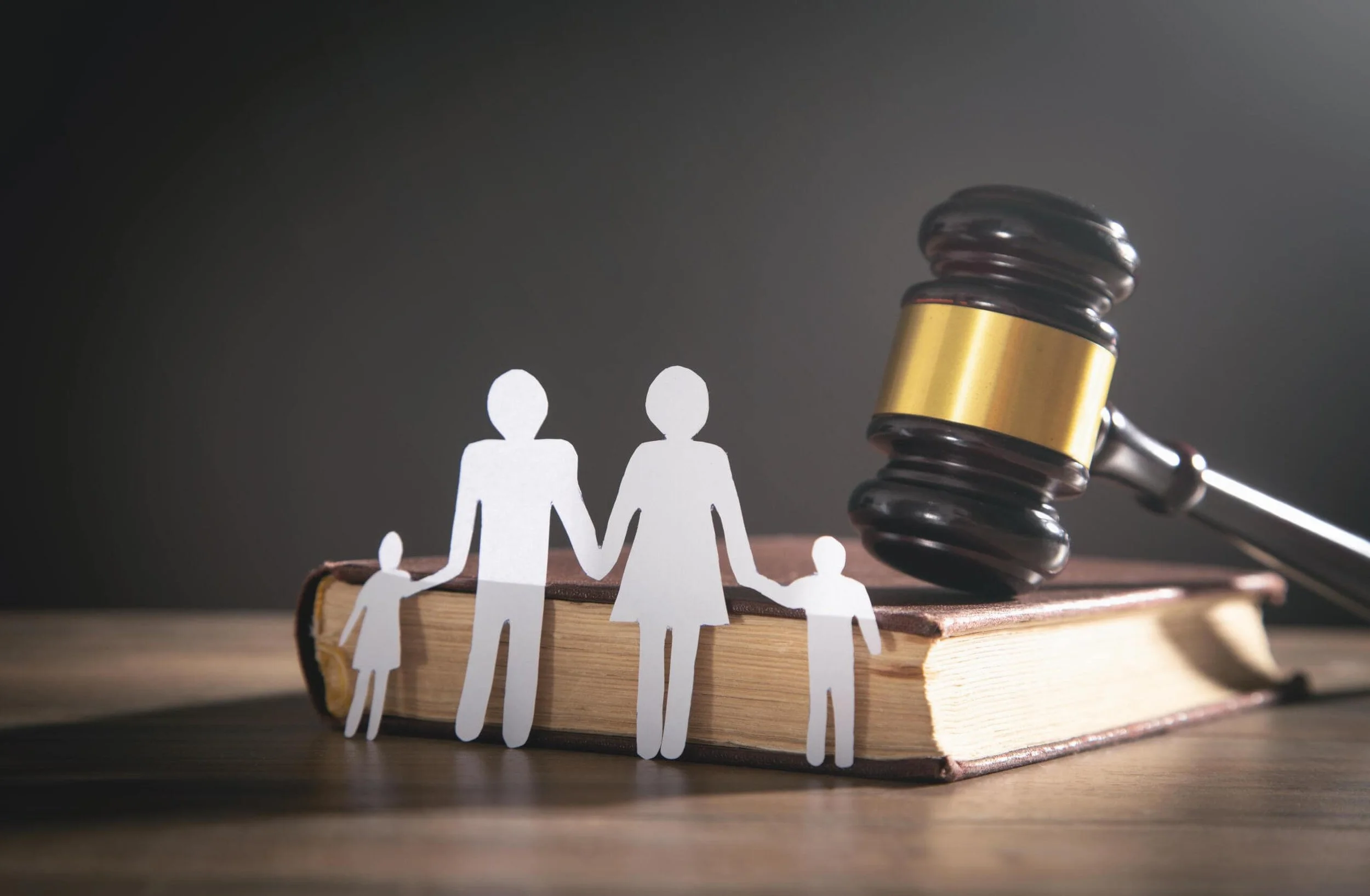 Paper cutout family holding hands on a book, with a gavel nearby, symbolizing legal issues related to families or family law.