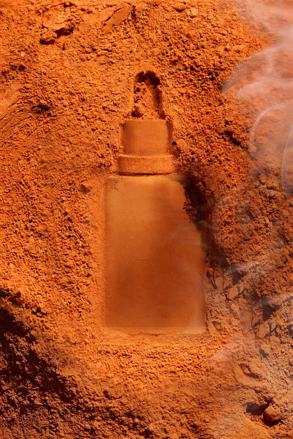 A small bottle-shaped object partially buried in orange dirt.