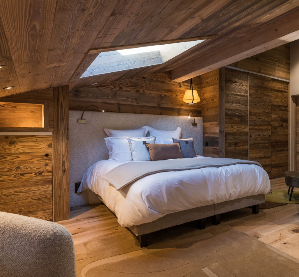 Chambre à coucher avec un lit douillet et une tête de lit sur mesure en tissu bouclette, lampes murales, mobilier en bois, sous un plafond en pente avec un velux.