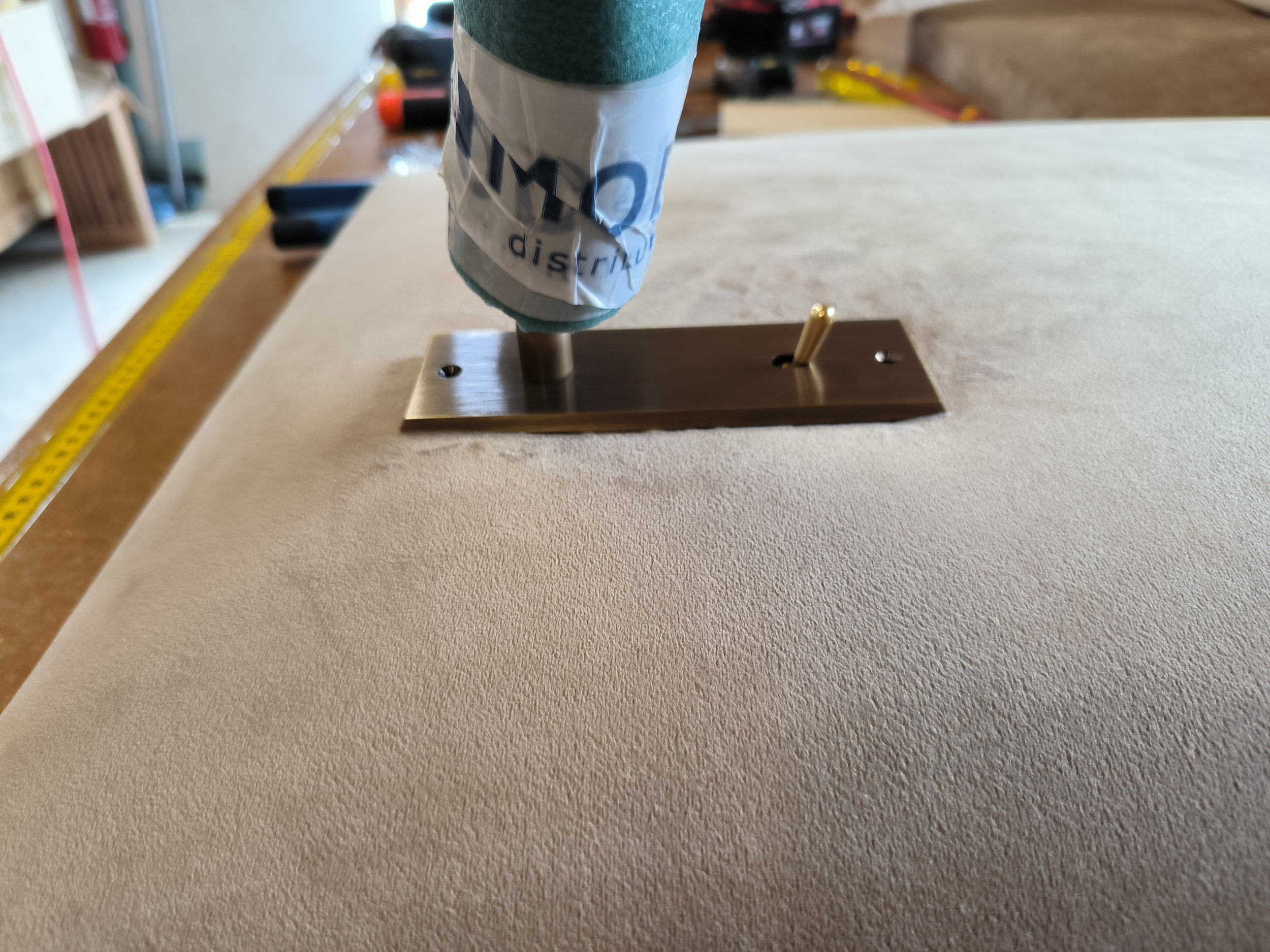 Une liseuse en cours d'installation sur une tête de lit en velours beige. En arrière-plan, il y a une règle de mesure jaune et des outils ou outils électriques.