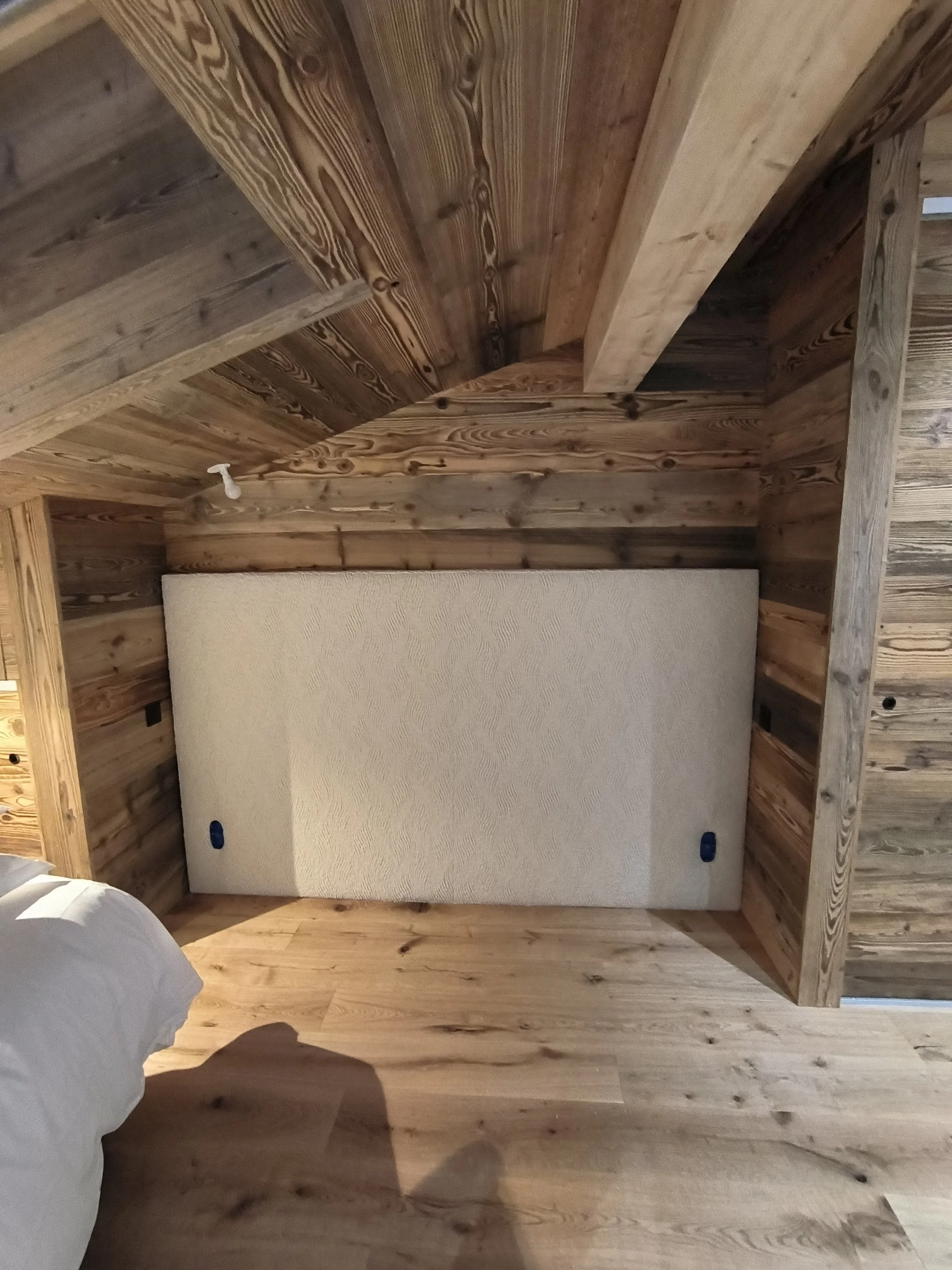 Un lit avec une tête de lit en tissu bouclette dans une chambre à plafond en bois.