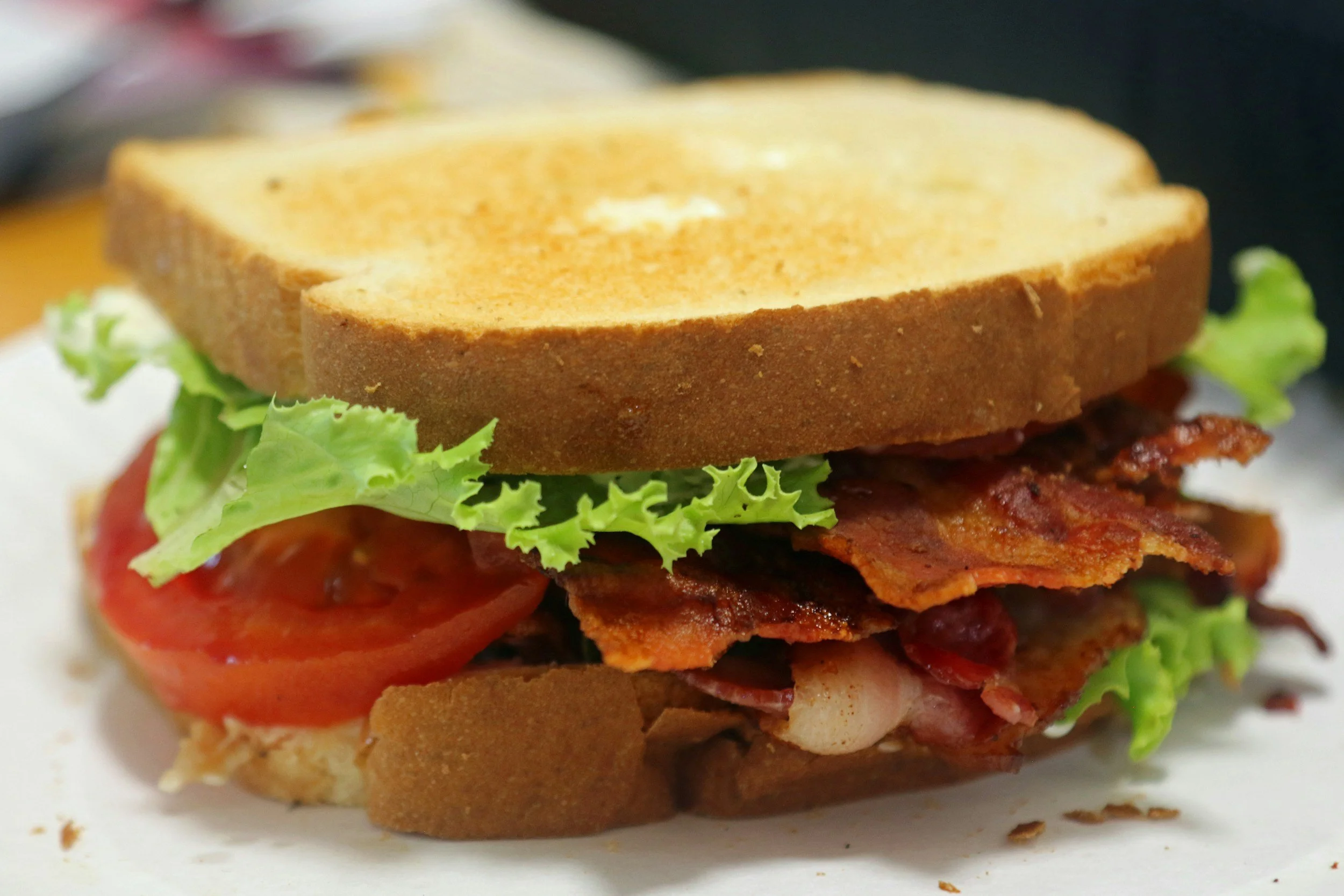 Close-up of a sandwich with layers of bacon, tomato, lettuce, and bread slices.