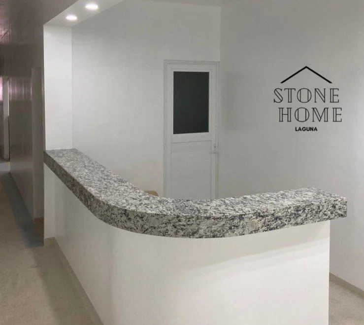 Barra de granito en forma curva en una pared blanca, con un cartel que dice 'Stone Home Laguna' en la pared.