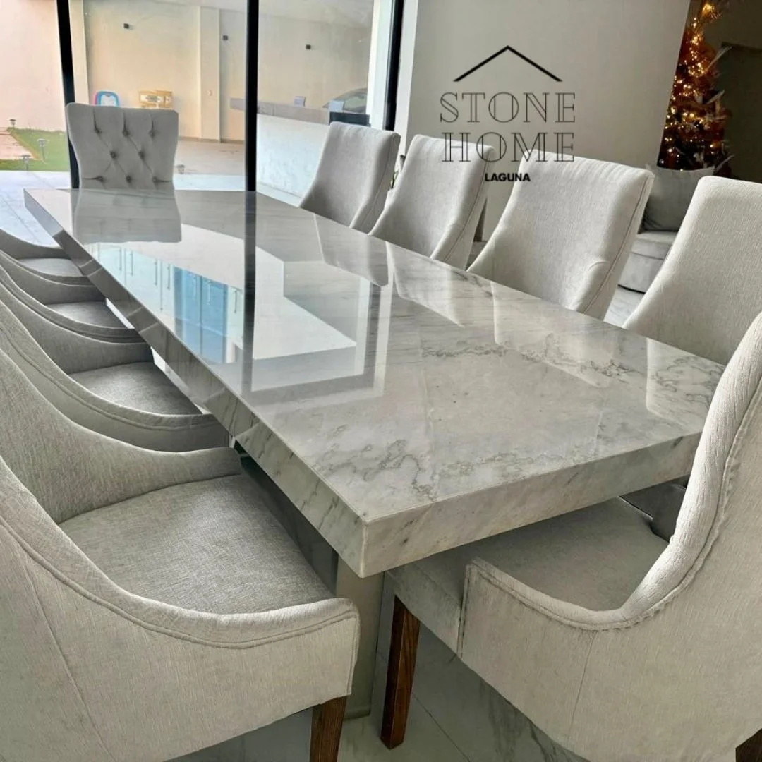 Mesa de comedor de mármol con sillas tapizadas de beige. Puerta de cristal y árbol de Navidad decorado en el fondo.