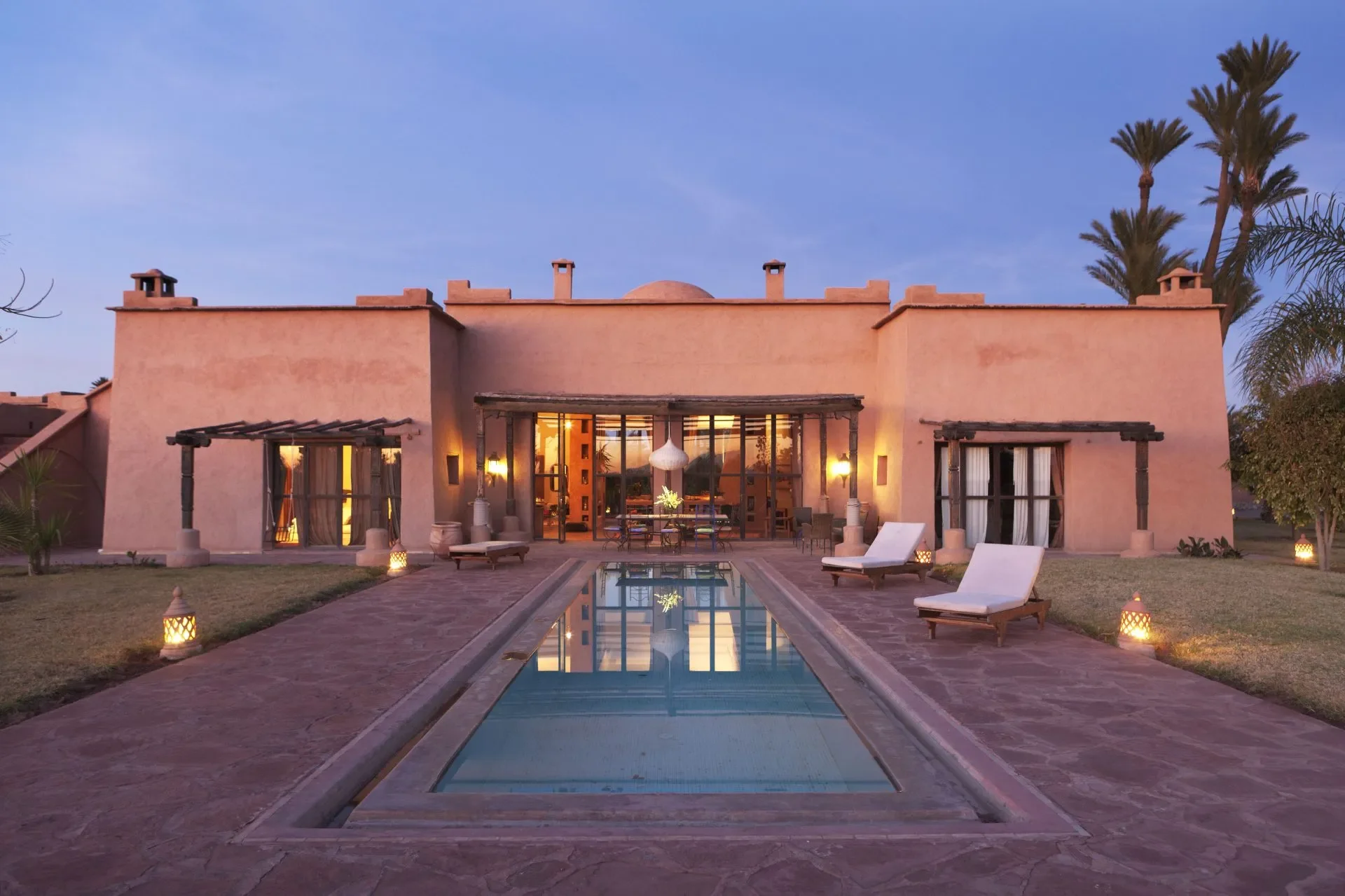Casa de estilo árabe en la noche, con iluminación exterior y una piscina en el patio, rodeada de palmeras.