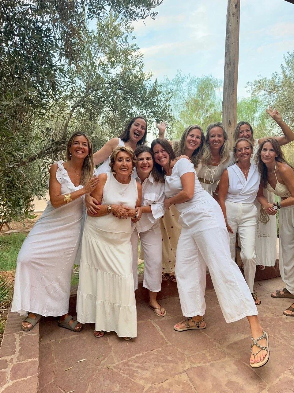 Grupo de mujeres sonriendo y posando juntas en un entorno natural, todas vestidas con ropa blanca.
