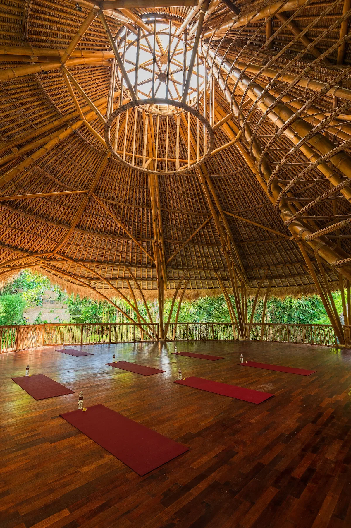 Interior de una estructura de techo de bambú con vistas a un área de yoga con alfombrillas y botellas de agua.