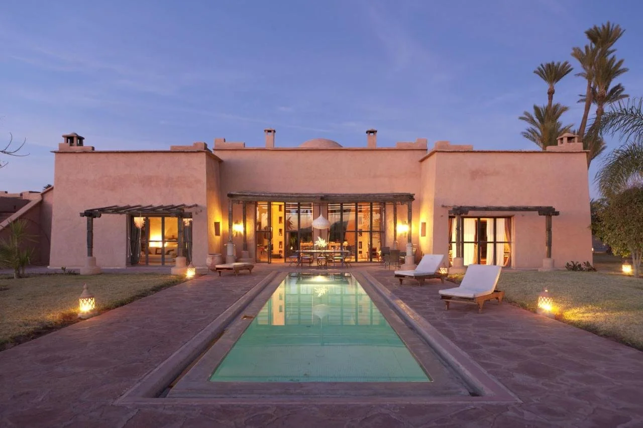 Casa moderna de estilo árabe con piscina en el patio y palmeras al fondo durante el atardecer.