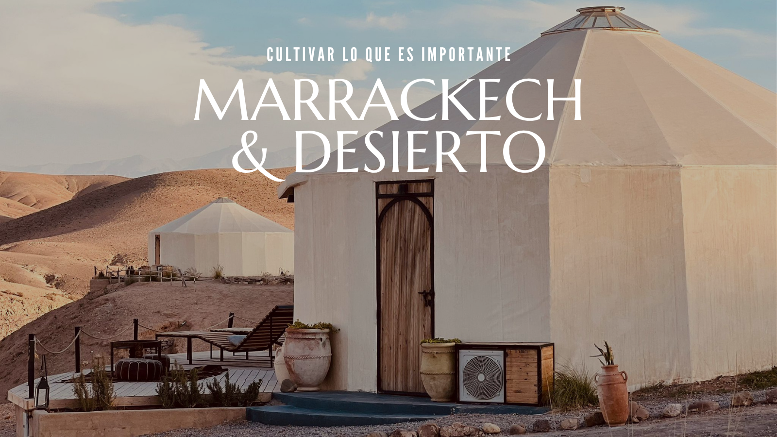 Casa blanca en el desierto de Marrakech con muebles y plantas decorativas, cielos despejados y montañas en el horizonte.