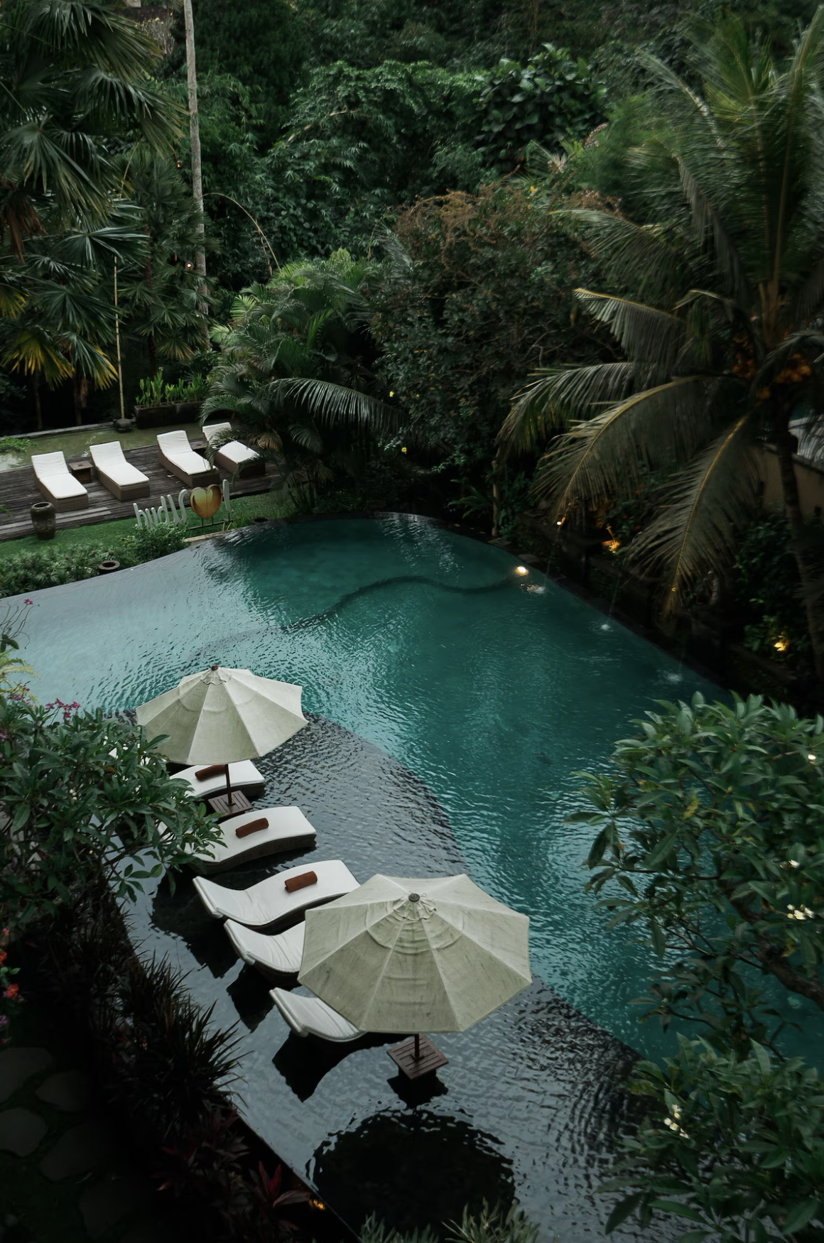 Piscina con tumbonas, sombrillas y vegetación tropical en un entorno de resort.