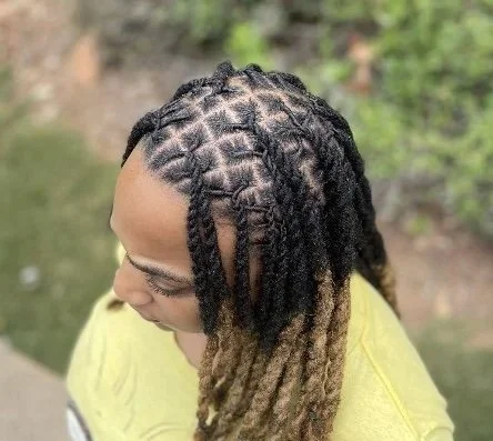 Top view of a person with styled braided hair and dreadlocks, wearing a yellow shirt.