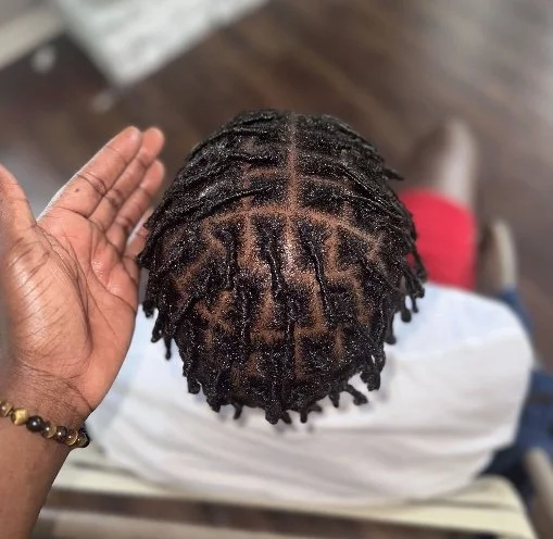 Top-down view of a person's head with freshly styled black dreadlocks, with a part in the center.
