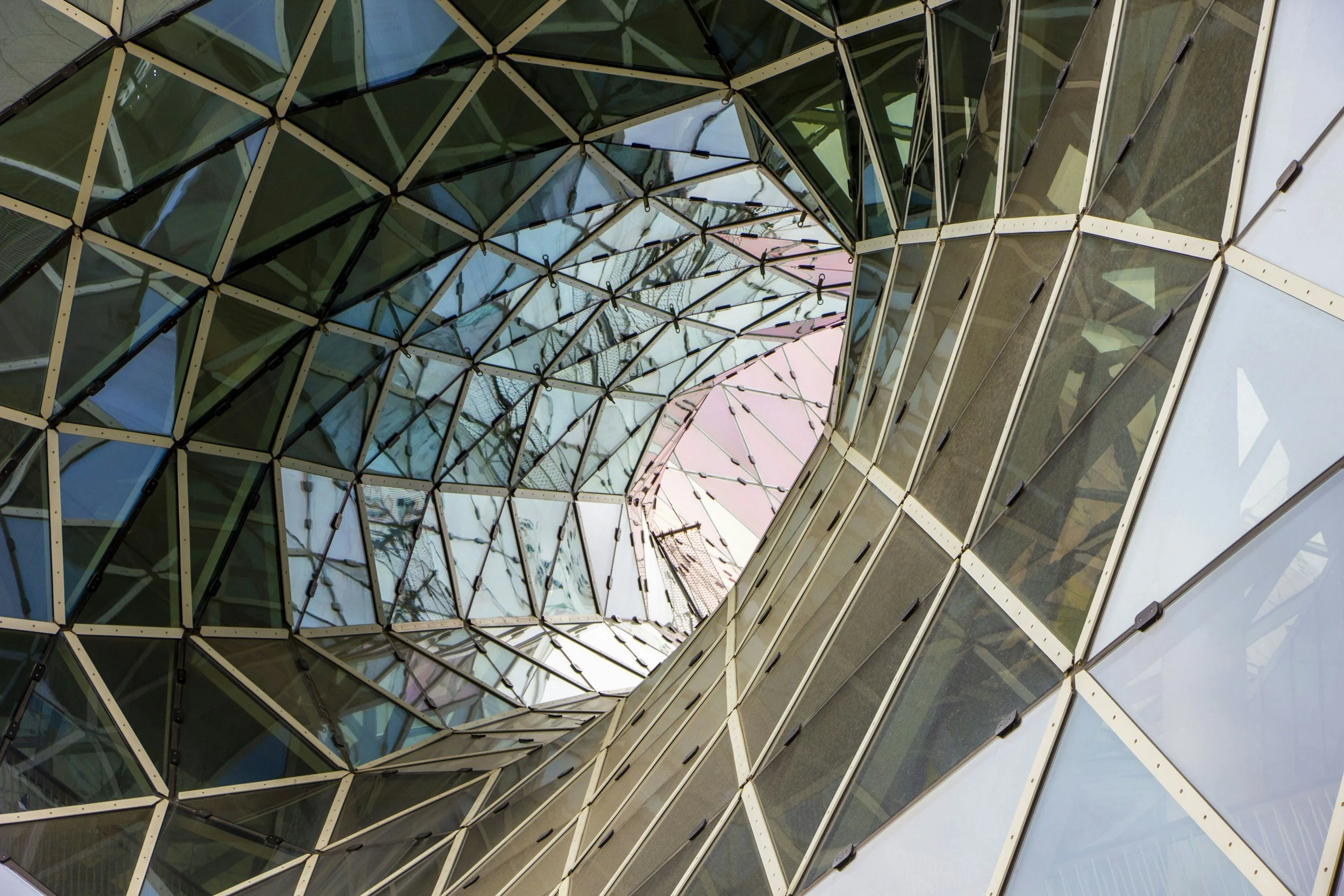 Looking up at a modern glass building with a spiraling, geometric facade.