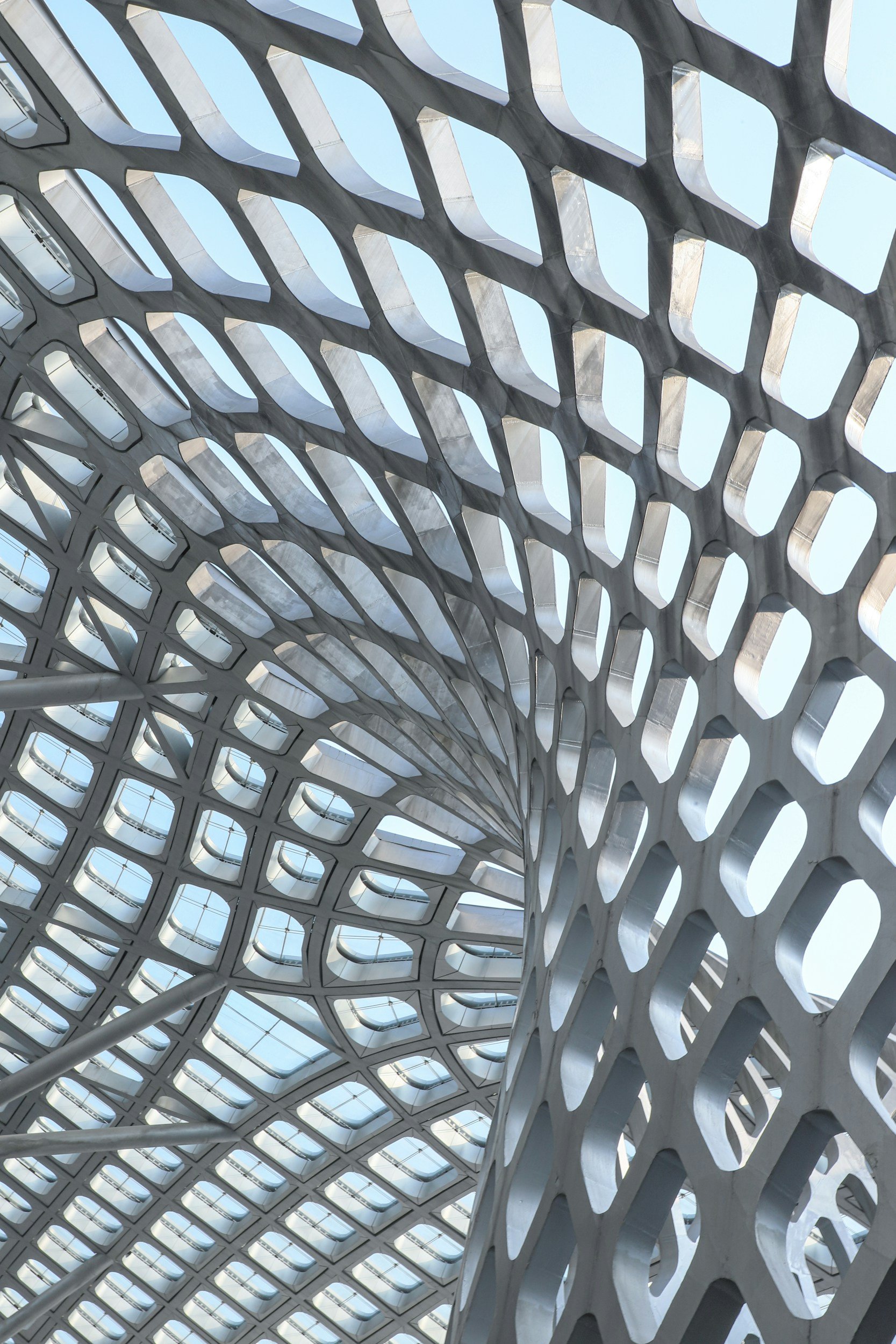 Interior view of a modern architectural structure with a geometric metal lattice ceiling, allowing natural light to filter through the openings.