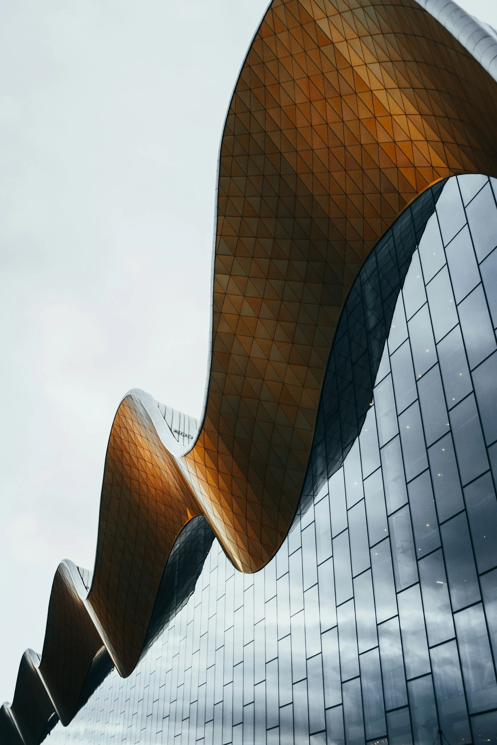 Parametric building architecture with curved undulating roof and glass facade reflecting the sky.