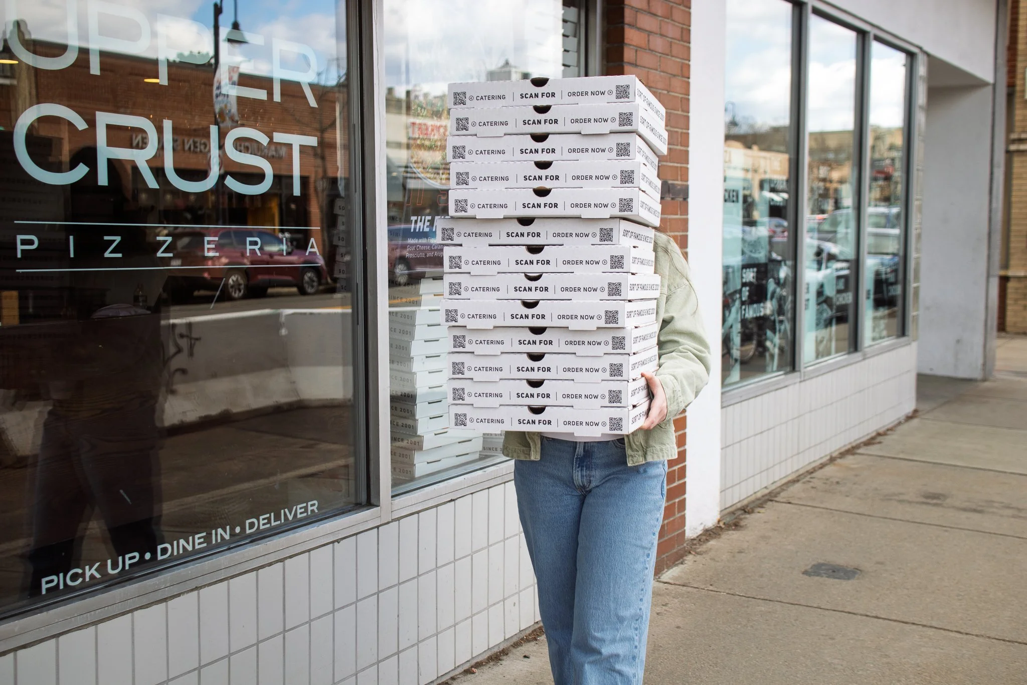 Woman holding a stack of pizza boxes outside an Upper Crust