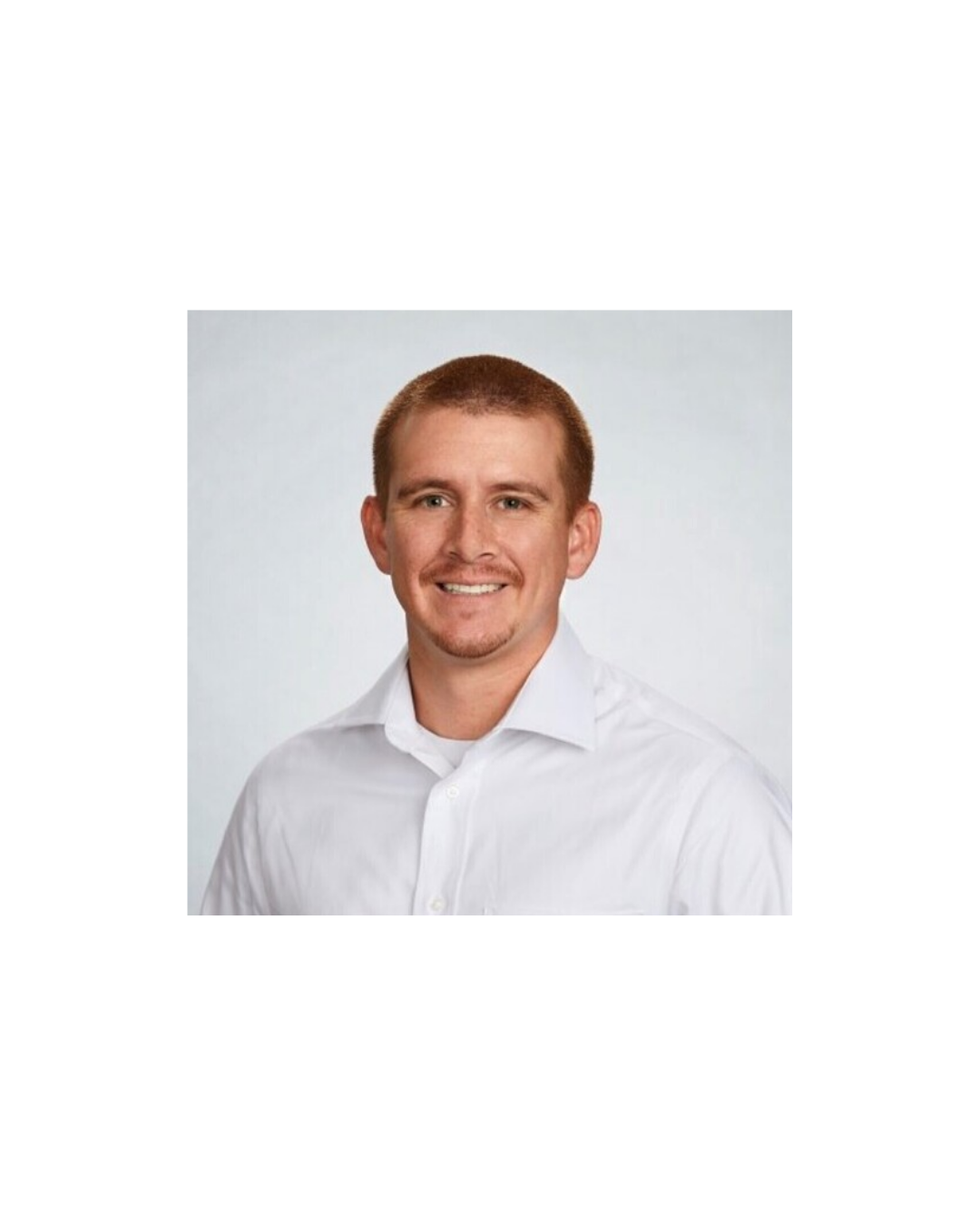 Portrait of a young man with short brown hair, wearing a white collared shirt, smiling against a plain background.