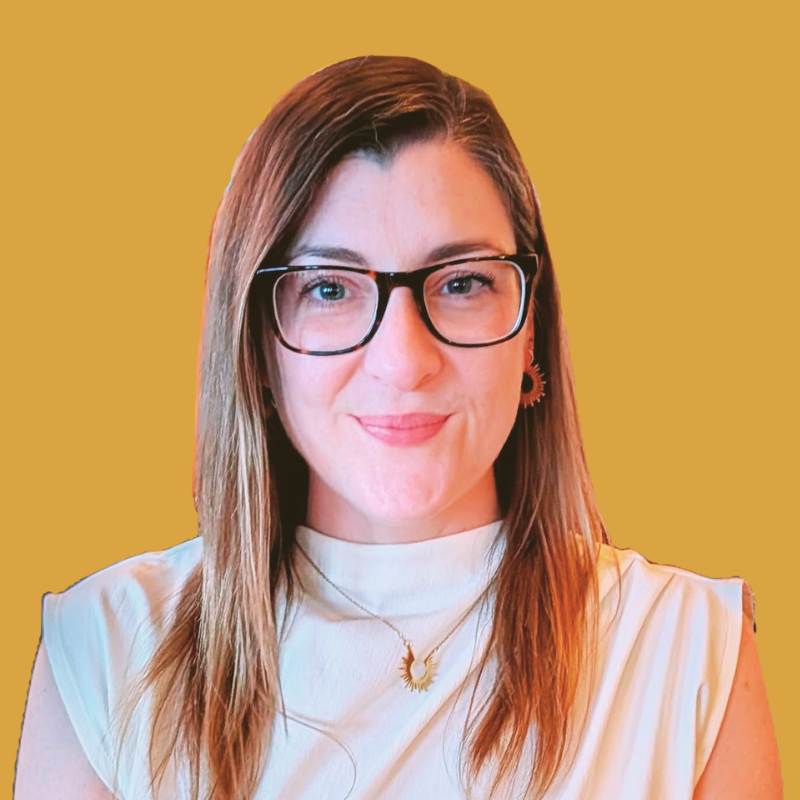 A woman with long straight hair, wearing black-rimmed glasses, a white top, and gold jewelry, smiling against a mustard yellow background.