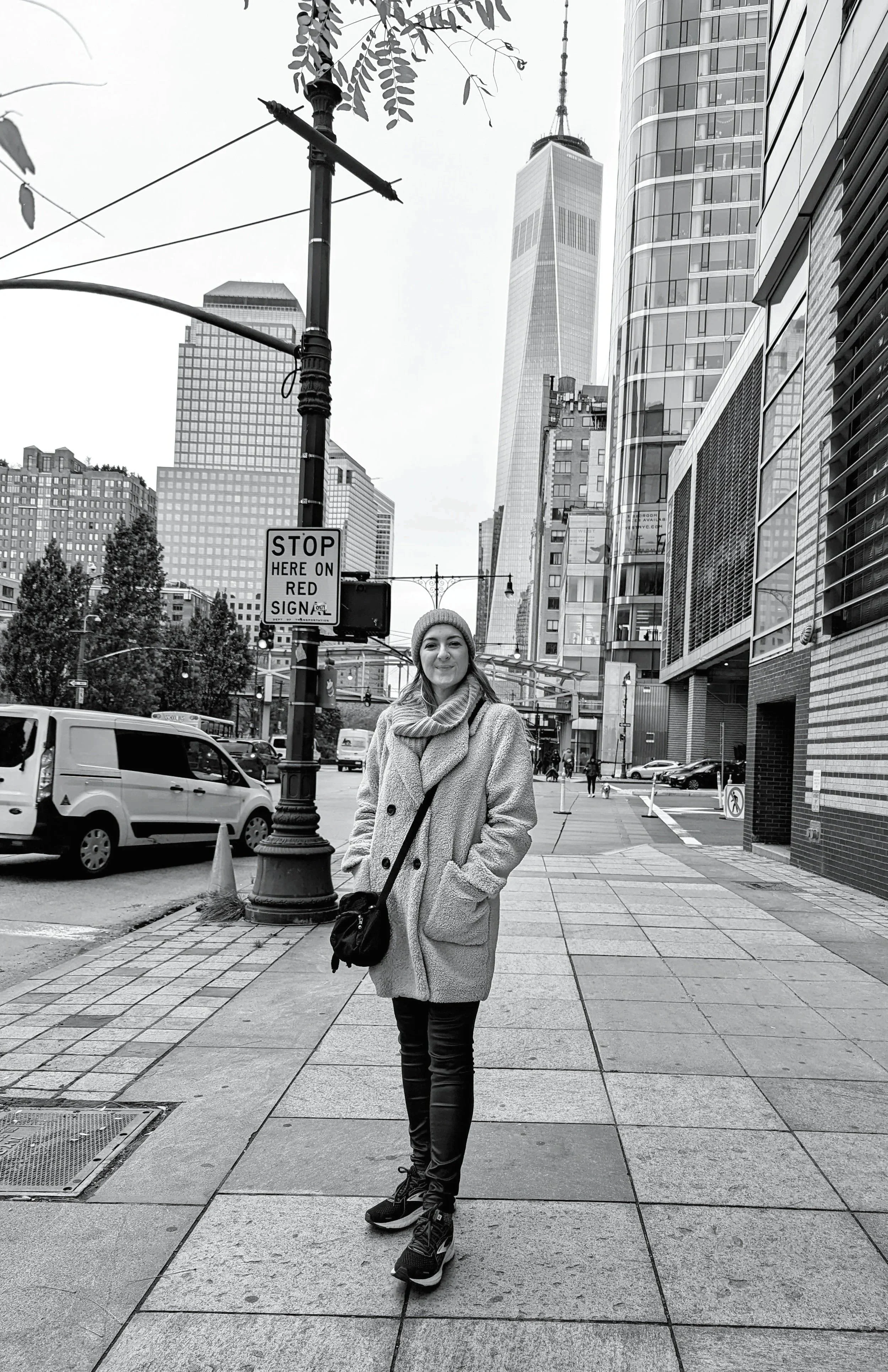 Jenny, the CEO of Cantrell Consulting, on a city sidewalk in front of tall modern buildings, wearing a coat, scarf, and hat, with a bag over her shoulder, smiling at the camera.