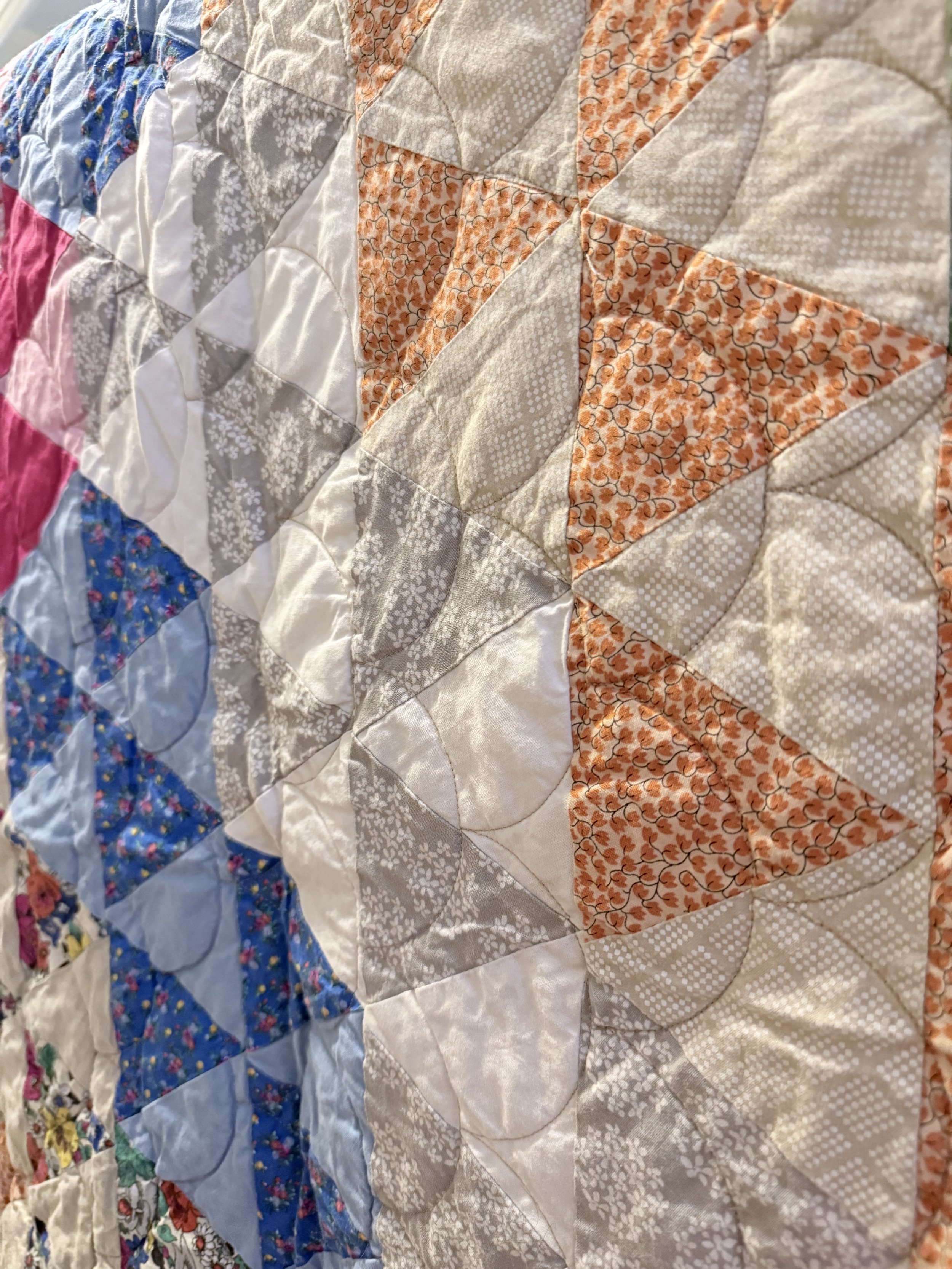 Close-up of a patchwork quilt with various fabric patterns, including floral, polka dots, and solid colors, stitched together in a geometric design.