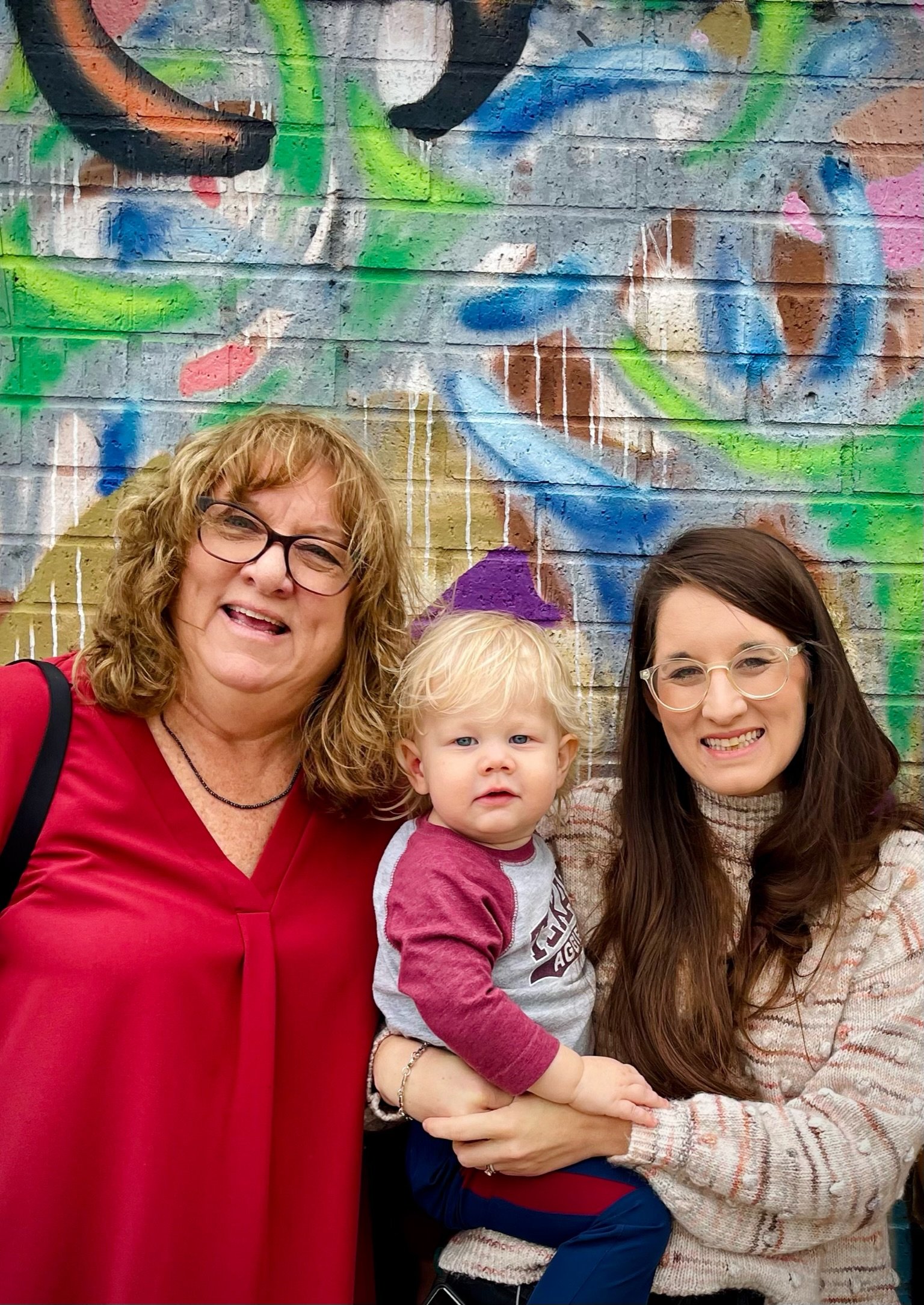 Group of three women and a young boy posing in front of a colorful graffiti wall.