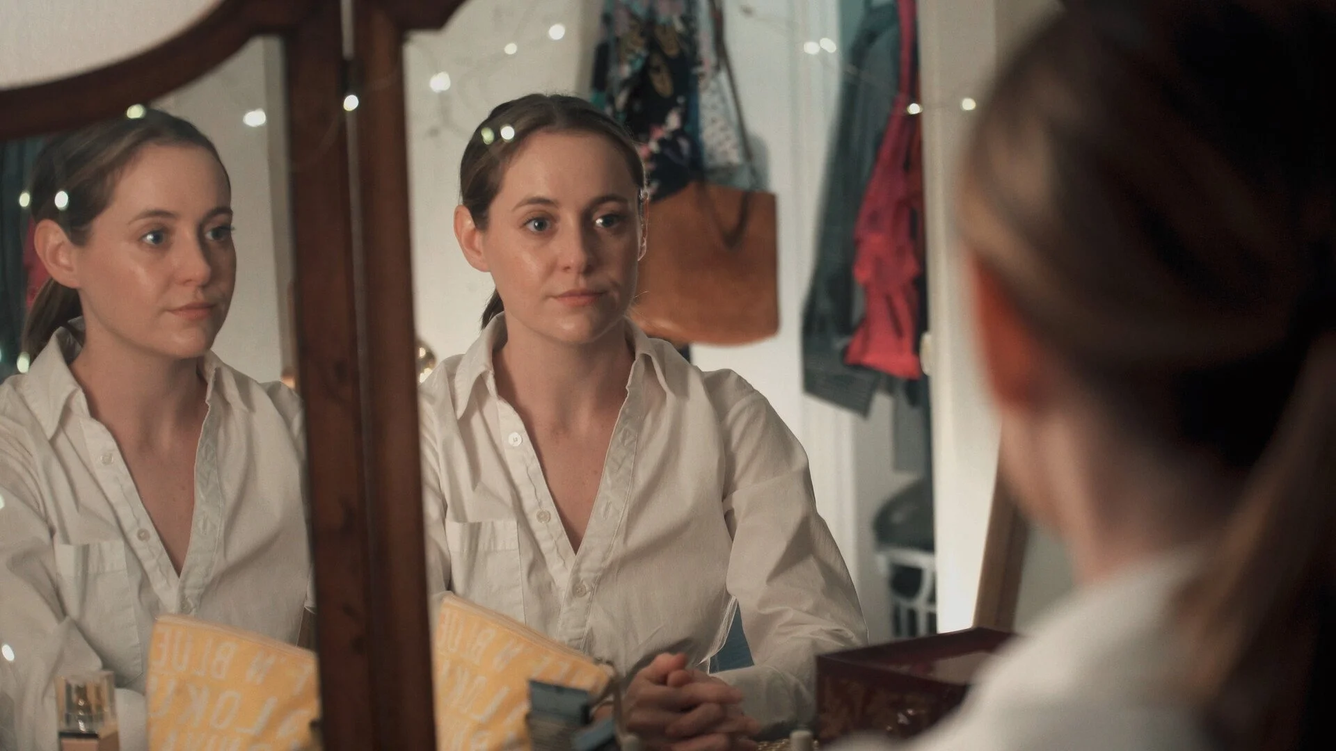  A still from the film "A Very Special Person." A woman in a white shirt looking at her reflection in a mirror, with a neutral expression. 