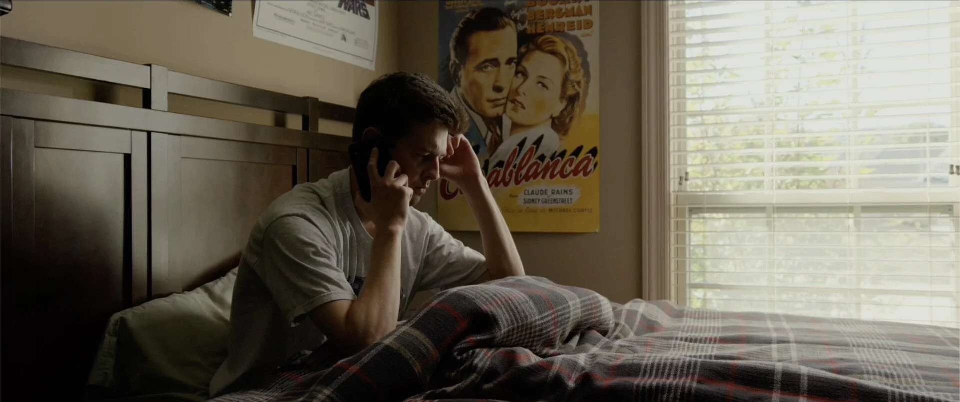 A still from the film "A Voicemail for Sarah." A young man sitting on a bed talking on a black phone. 