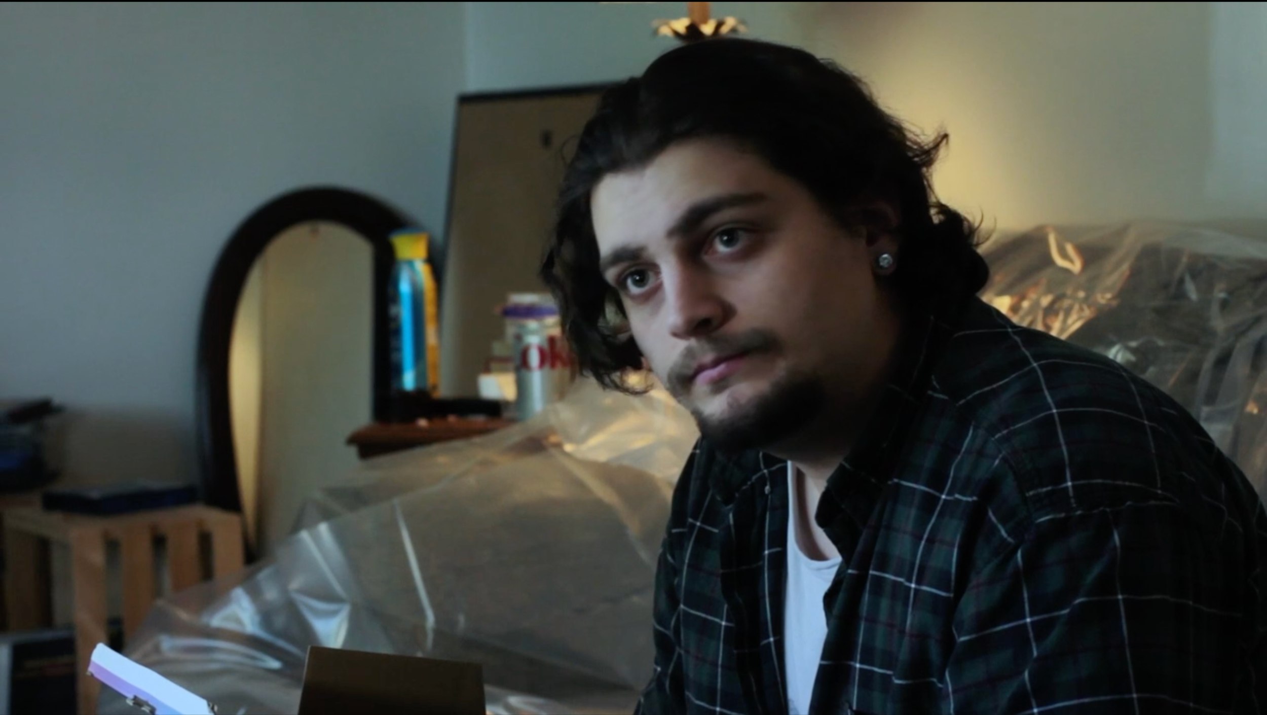 A still from the film "Tomorrow Is A Long Time.A young man with dark wavy hair sits indoors.