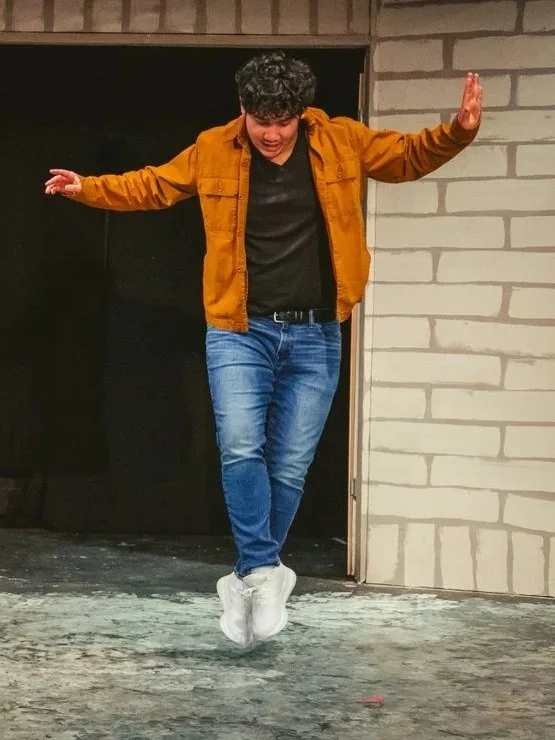 Actor jumping in the air with his arms out and feet crossed.