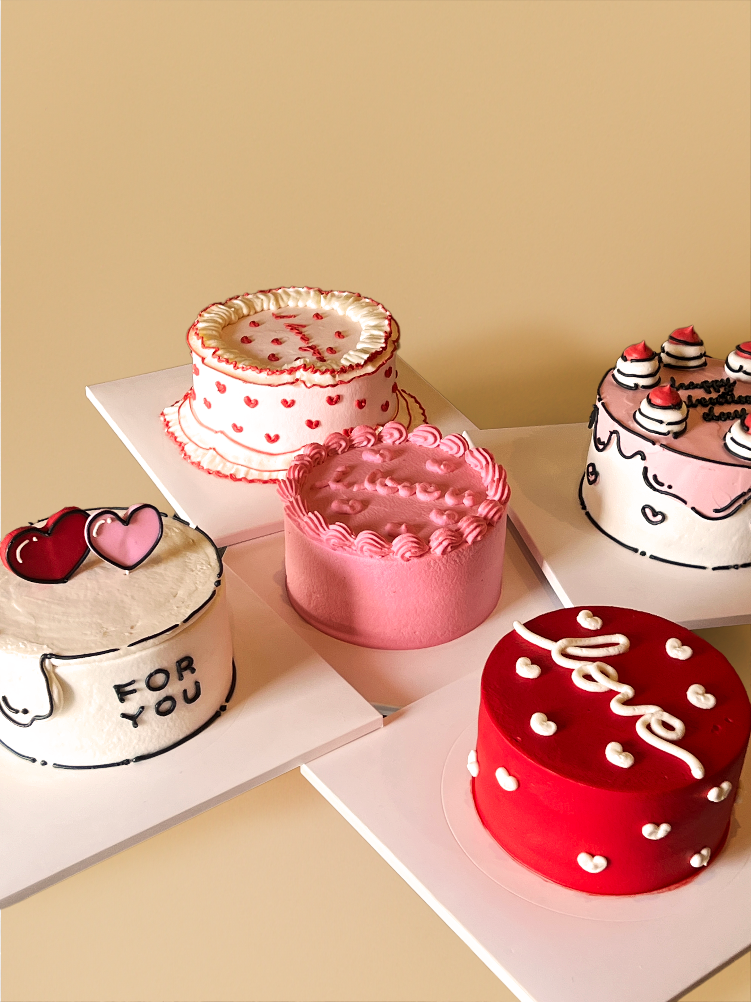 Collection of five decorated birthday cakes with pink, red, and white themes, featuring love and heart motifs.