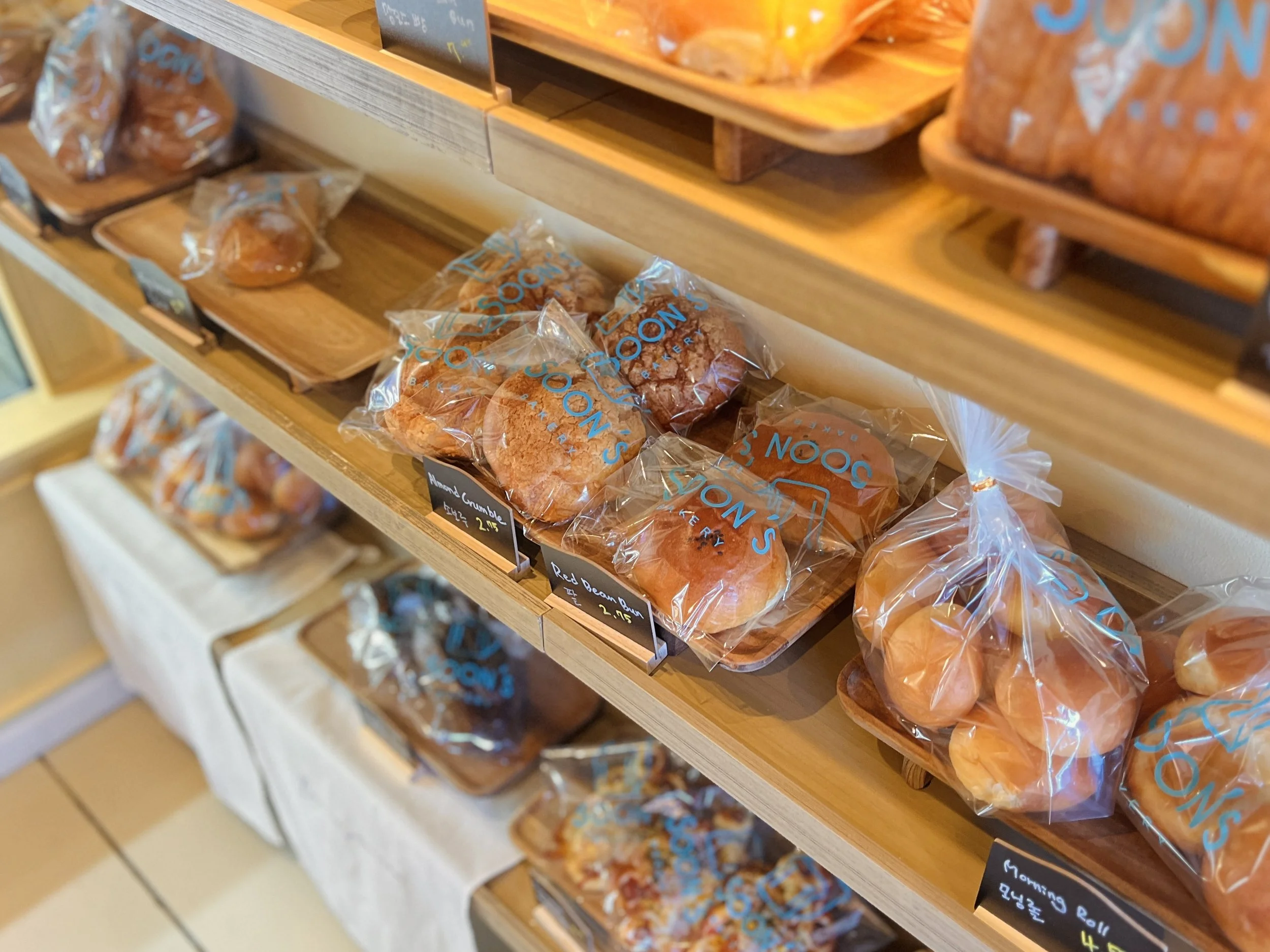 Bakery display shelves with various packaged baked goods, including rolls and bread, in a store.