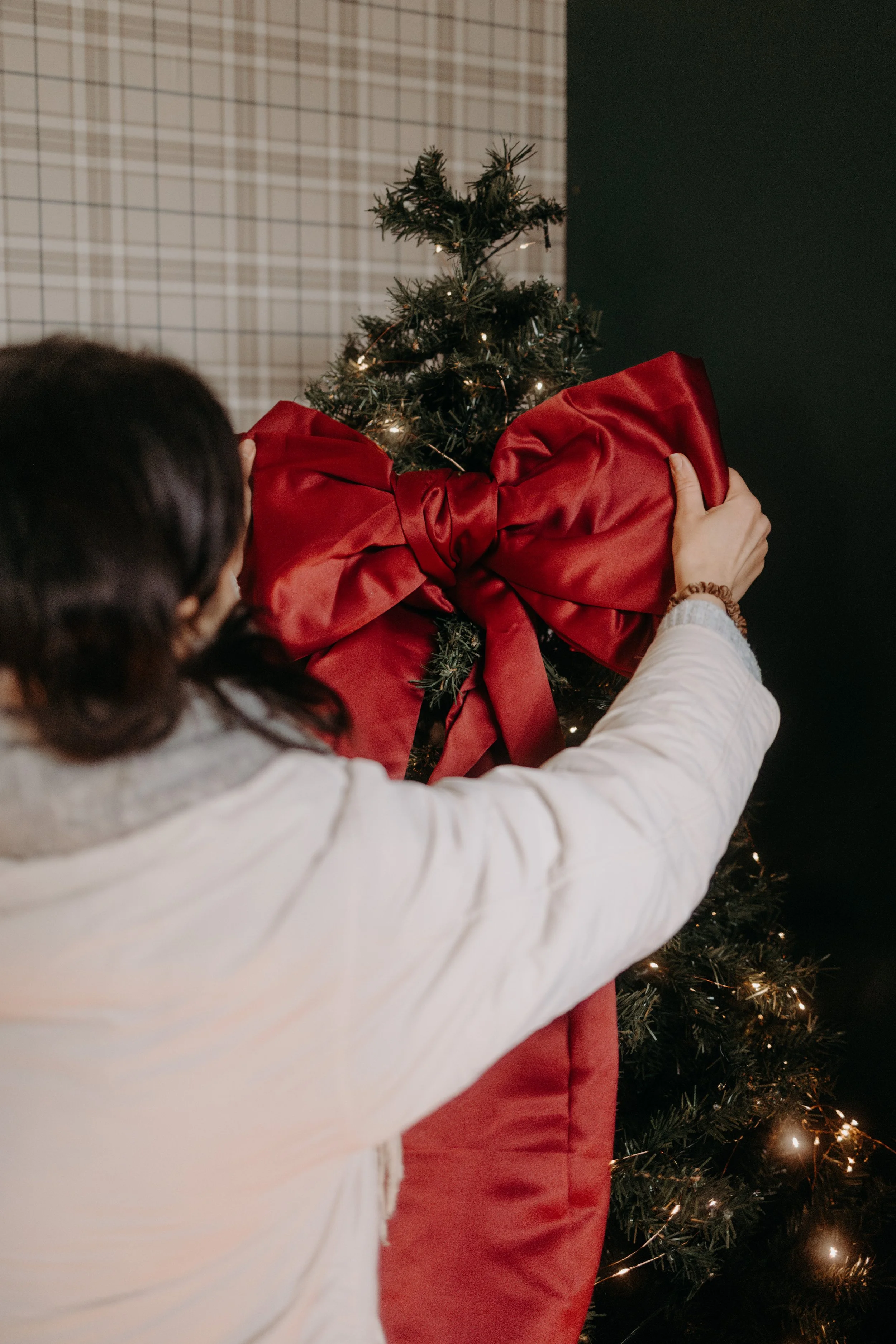 Une personne accroche une grande décoration en forme de nœud rouge sur un arbre de Noël.