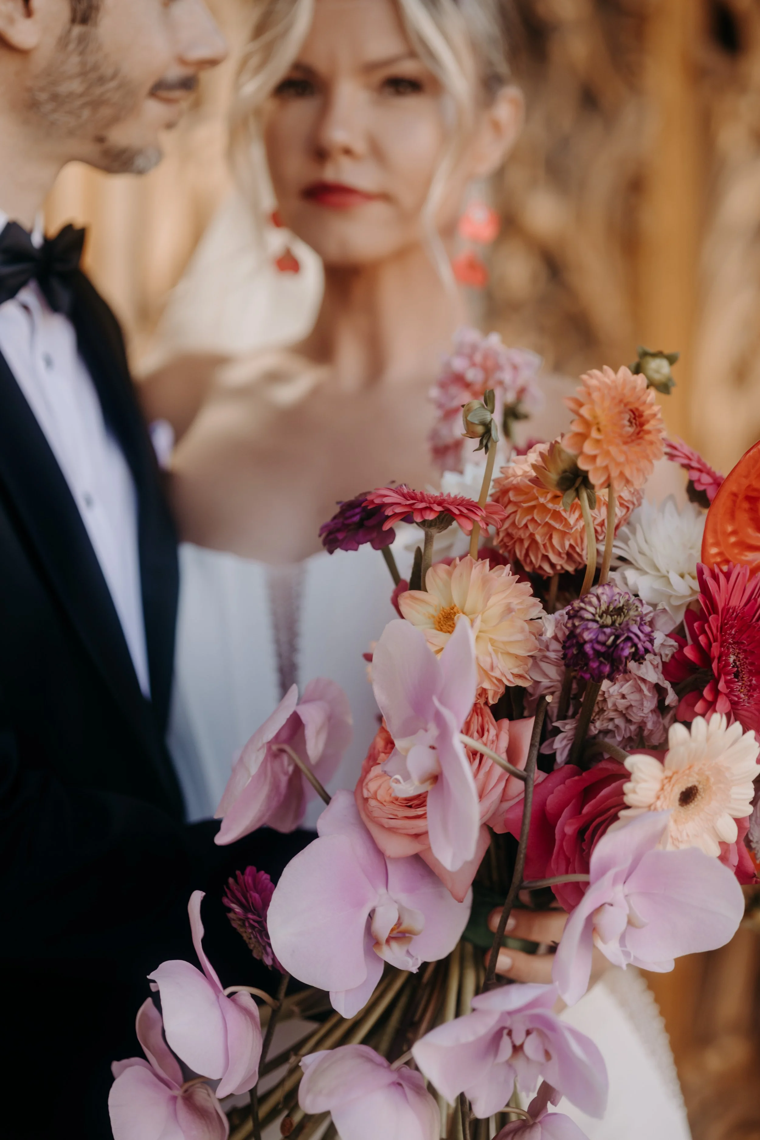 Un couple en tenue de mariage tenant un bouquet de fleurs colorées, avec une femme portant une robe blanche et un homme en smoking.