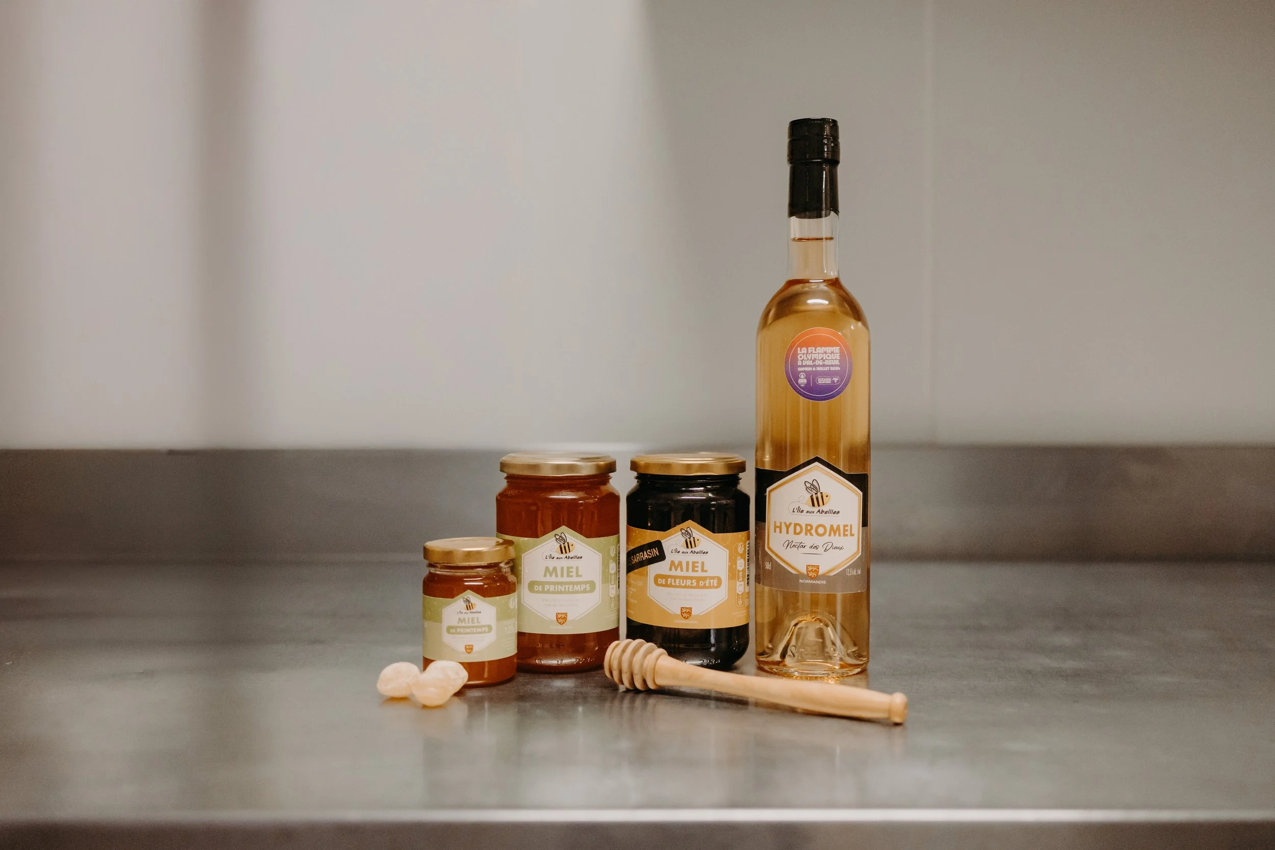 Miel, hydromel et accessoires sur une surface en métal, y compris un petit pot de miel, un pot de miel de fleurs d'été, un pot de miel de printemps, une bouteille de hydromel et une petite louche en bois.