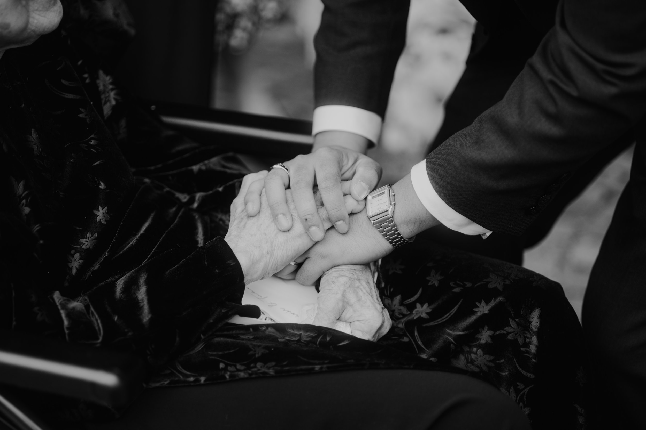 Deux mains se tiennent, une personne âgée dans un fauteuil roulant et une autre debout, lors d'une scène touchante.