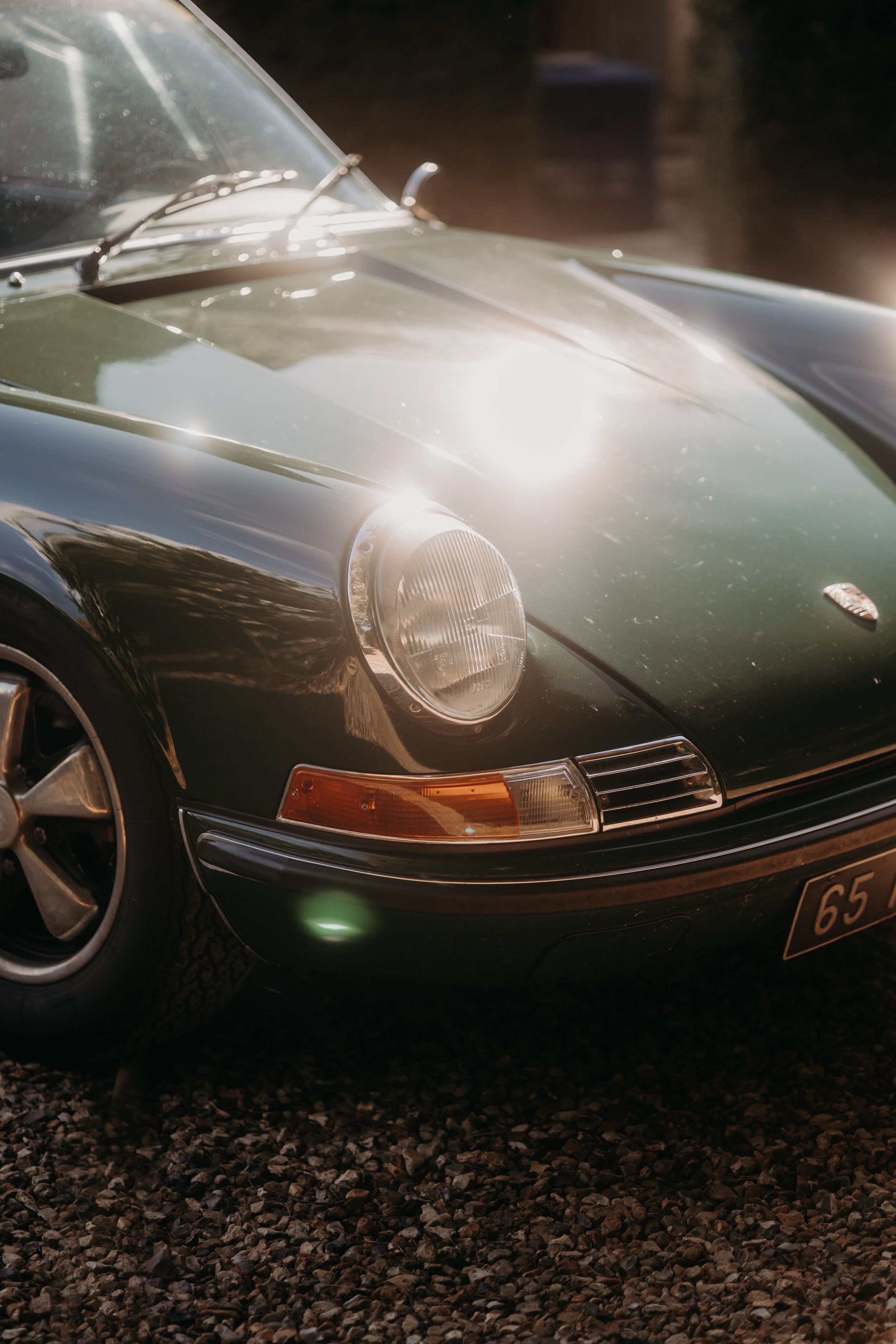 Premier plan d'une voiture ancienne de couleur verte, vue de côté, avec un phare rond et une lumière du soleil brillant sur la calandre.