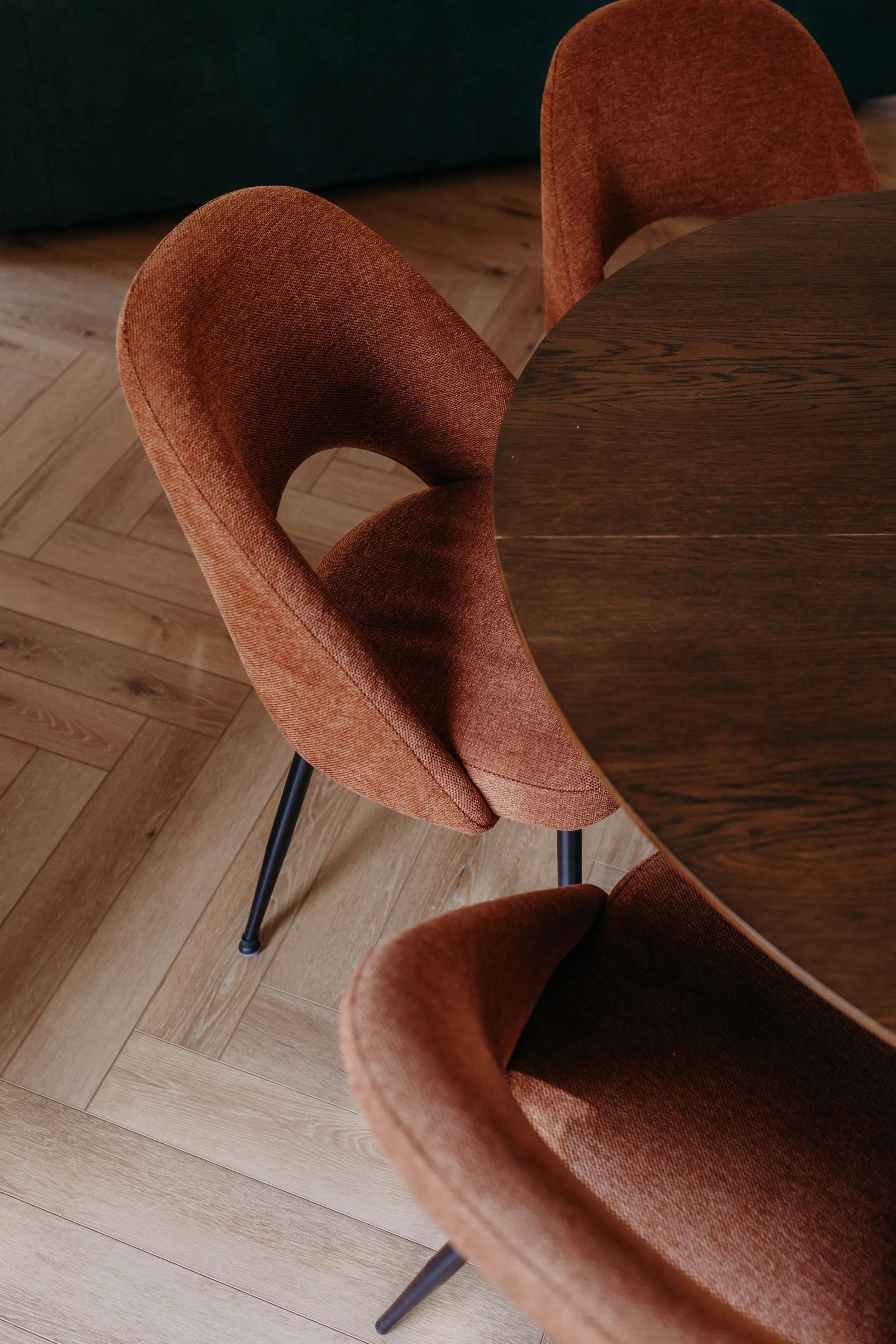 Vue d'une table ronde en bois avec trois chaises en velours orange dans une pièce avec un sol en parquet.