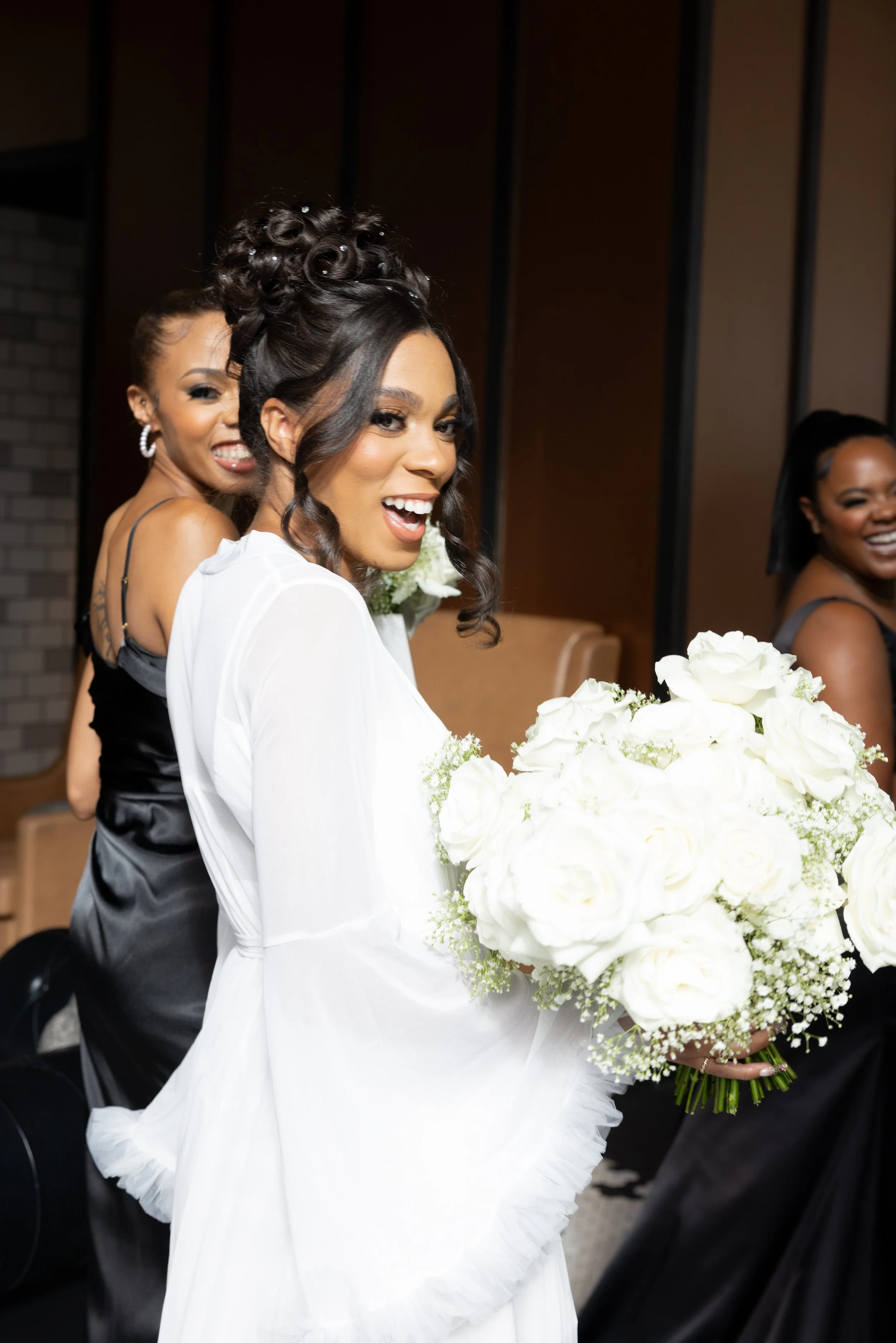Bridal party with the bride holding a large bouquet of white roses, smiling at a celebration.
