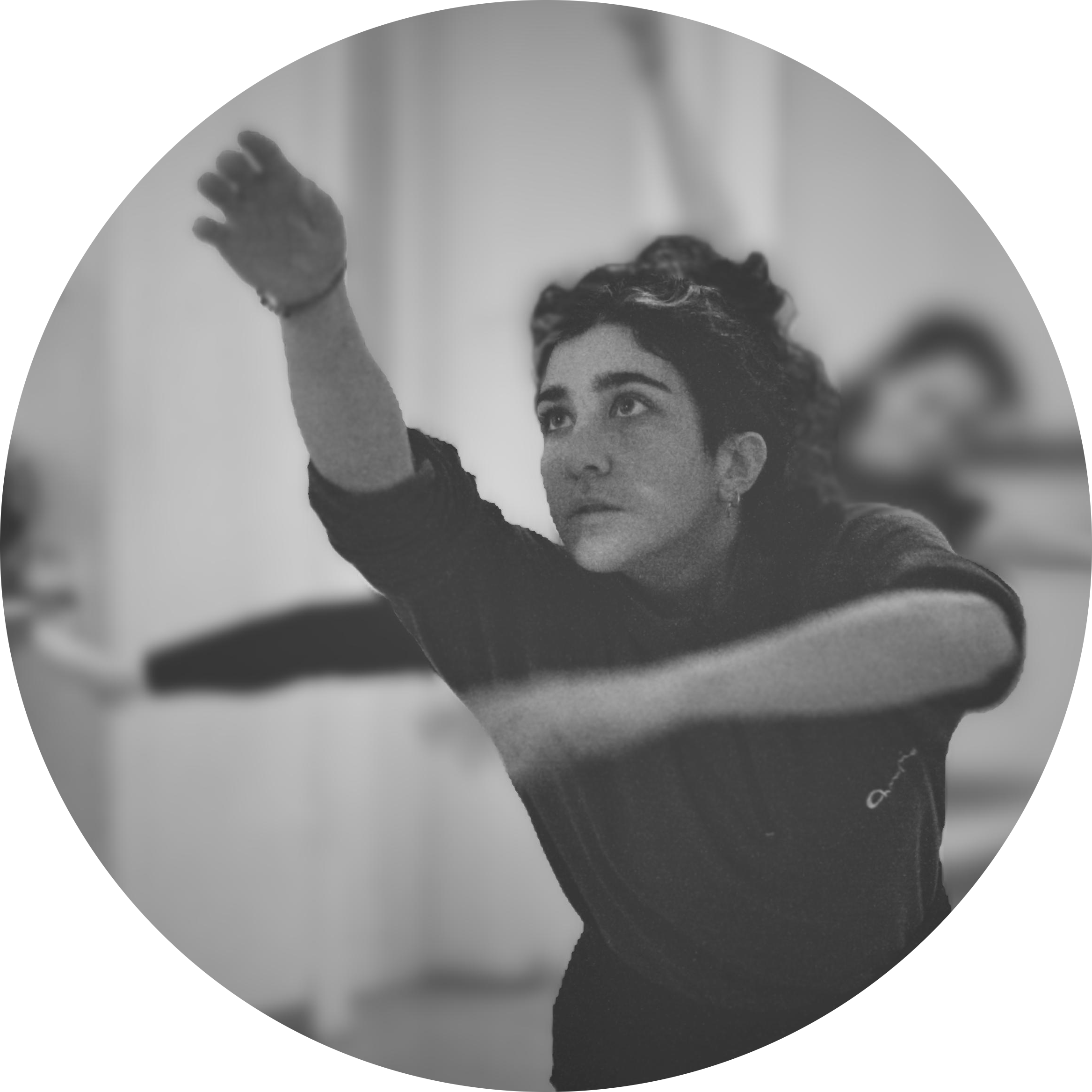 A woman with short, curly hair performing a dance move or exercise, with her arm extended upward, in a room with a blurred background.