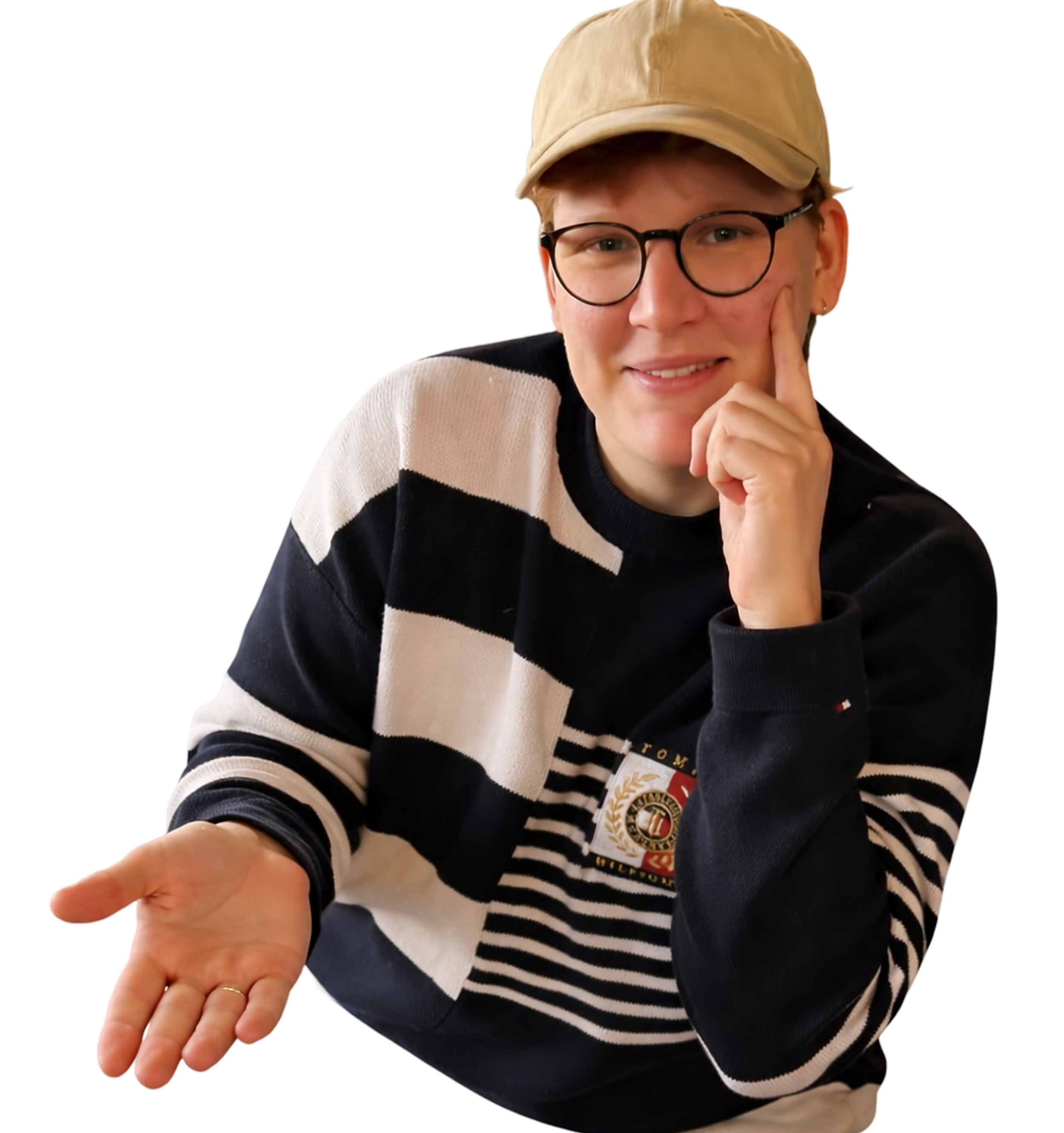 A person with short hair wearing glasses, a beige cap, and a black and cream striped sweater, with an emblem on the sweater, gestures with an open hand and touches their face with the other hand, smiling and looking at the camera.