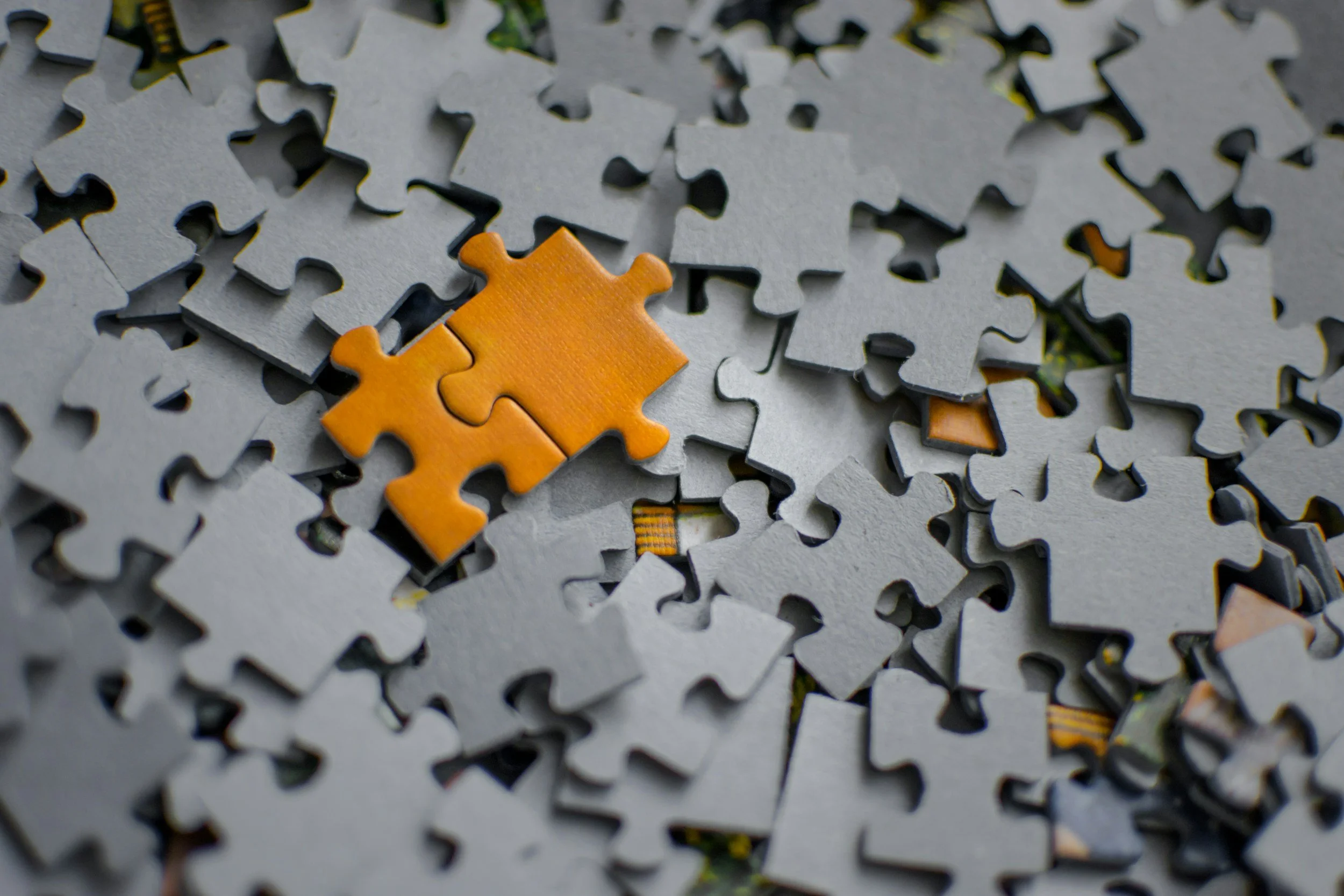 A scattered pile of unfinished jigsaw puzzle pieces with one orange piece in the center.